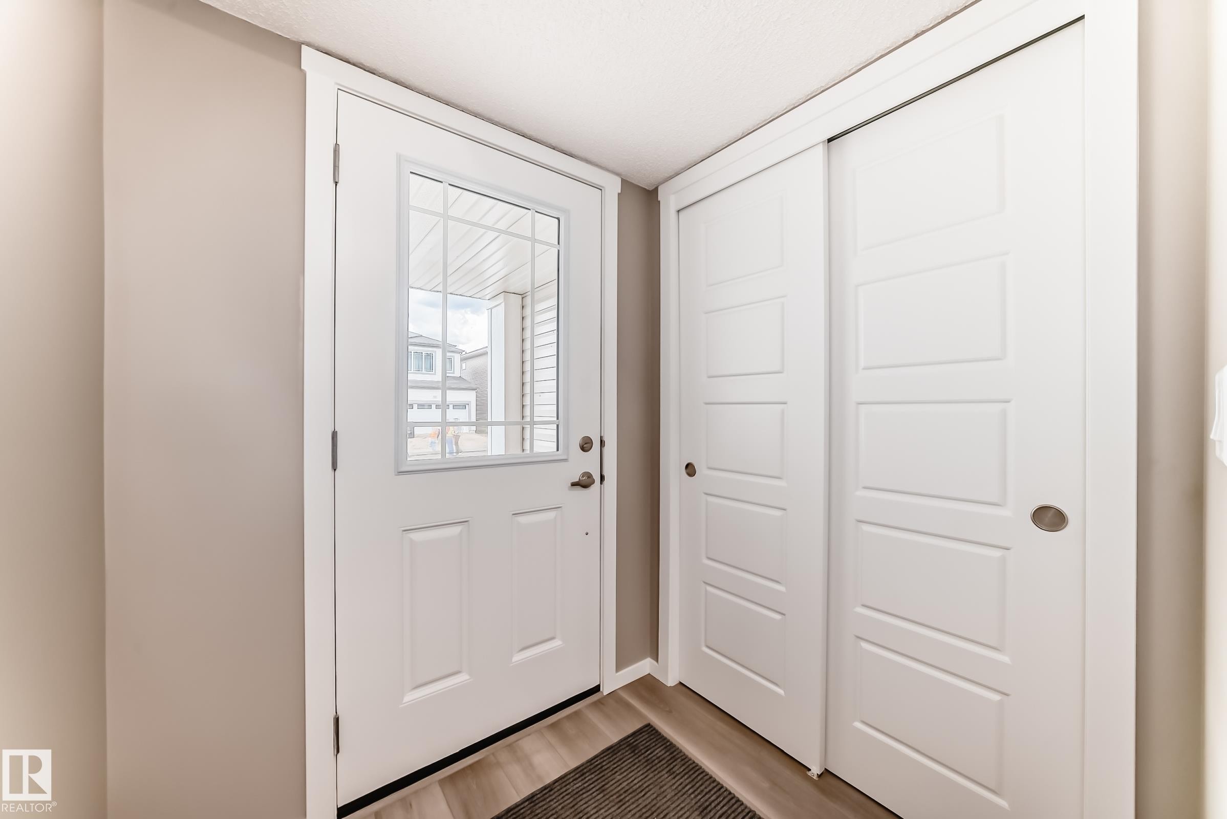 Entryway featuring a white door with upper window panes, adjacent to sliding closet doors with recessed paneling - 20415 16 Avenue, Edmonton, AB