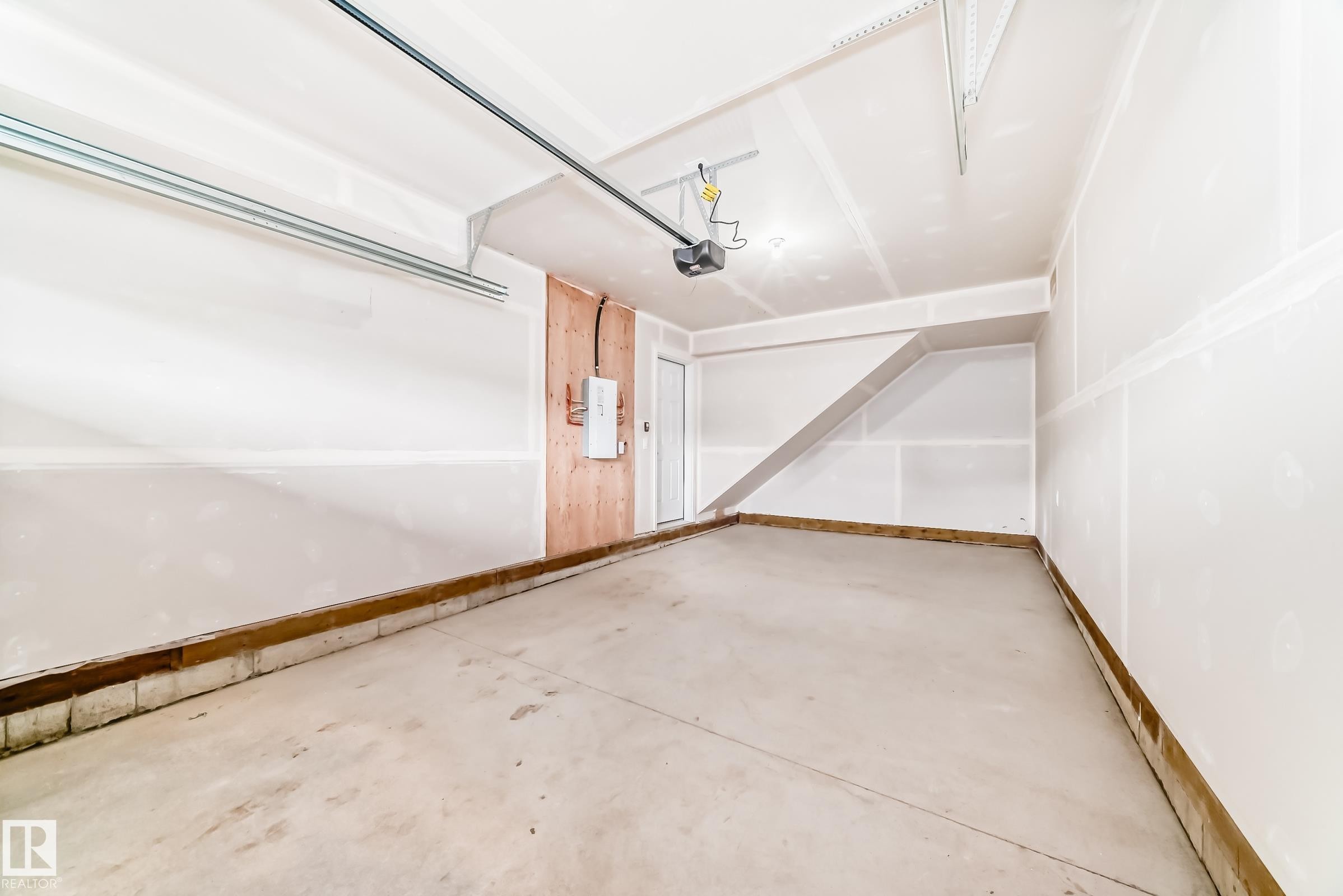 Spacious garage featuring a concrete floor, white drywall walls, ceiling-mounted garage door opener, and a utility panel on a wood-paneled section - 20415 16 Avenue, Edmonton, AB