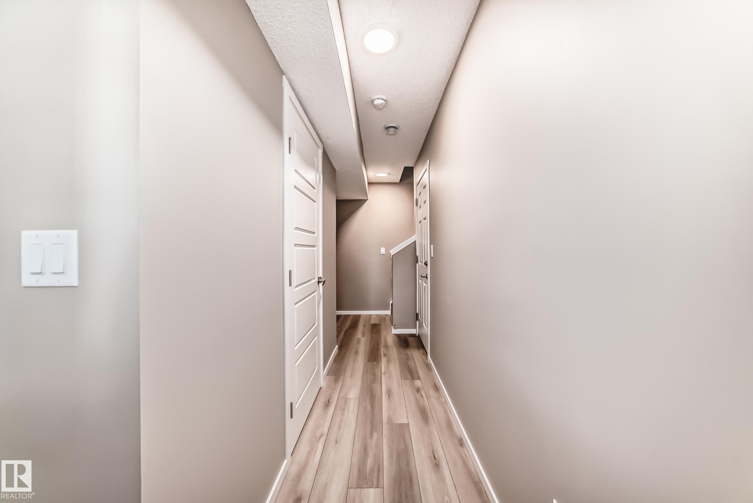 Hallway featuring wood-finish flooring, light neutral wall paint, and white trim - 20415 16 Avenue, Edmonton, AB