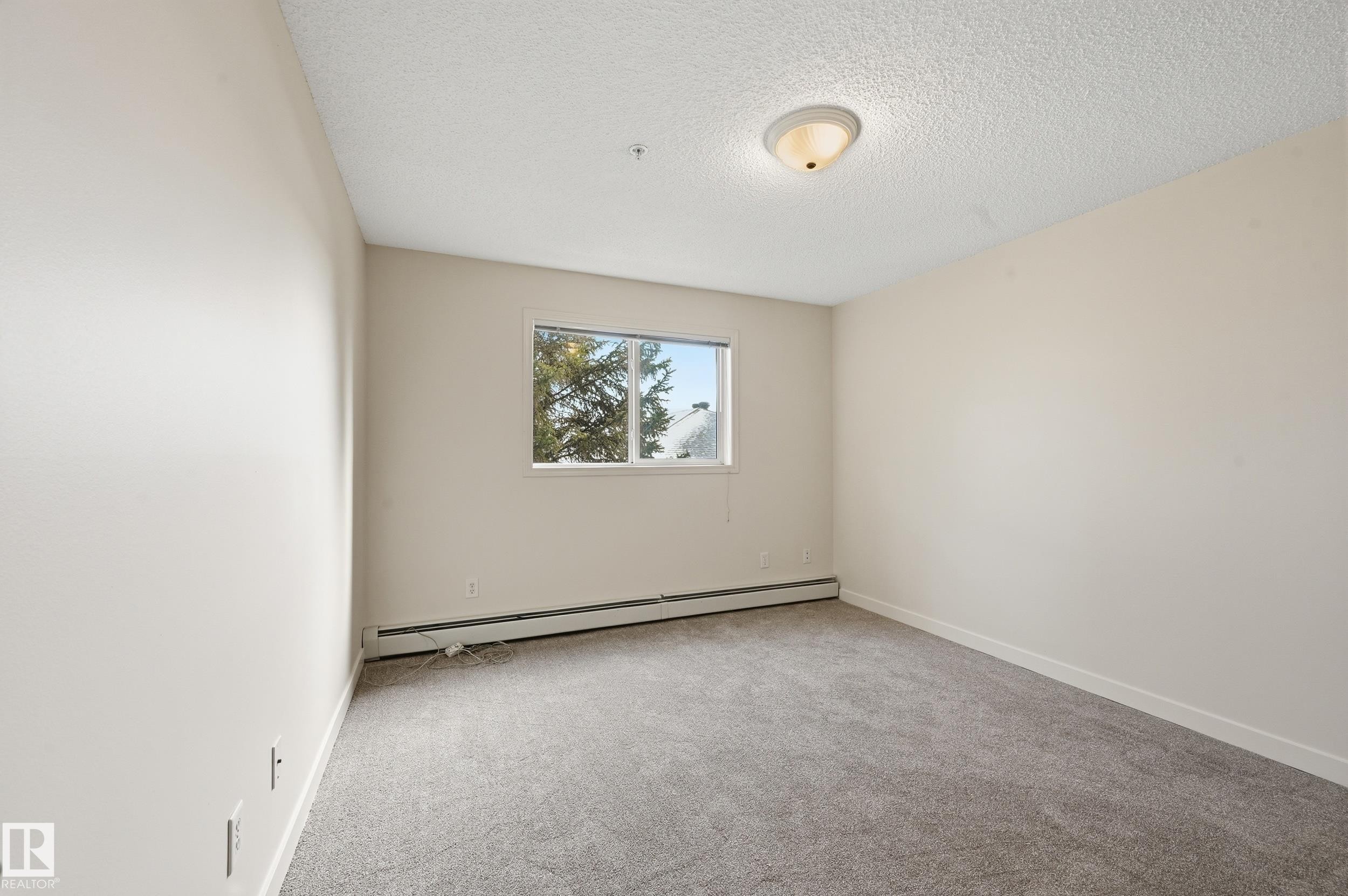 This room features light grey carpeting, white walls, and a window providing natural light and views of trees - 314 2430 Guardian Road, Edmonton, AB - Indoor Photo Showing Other Room