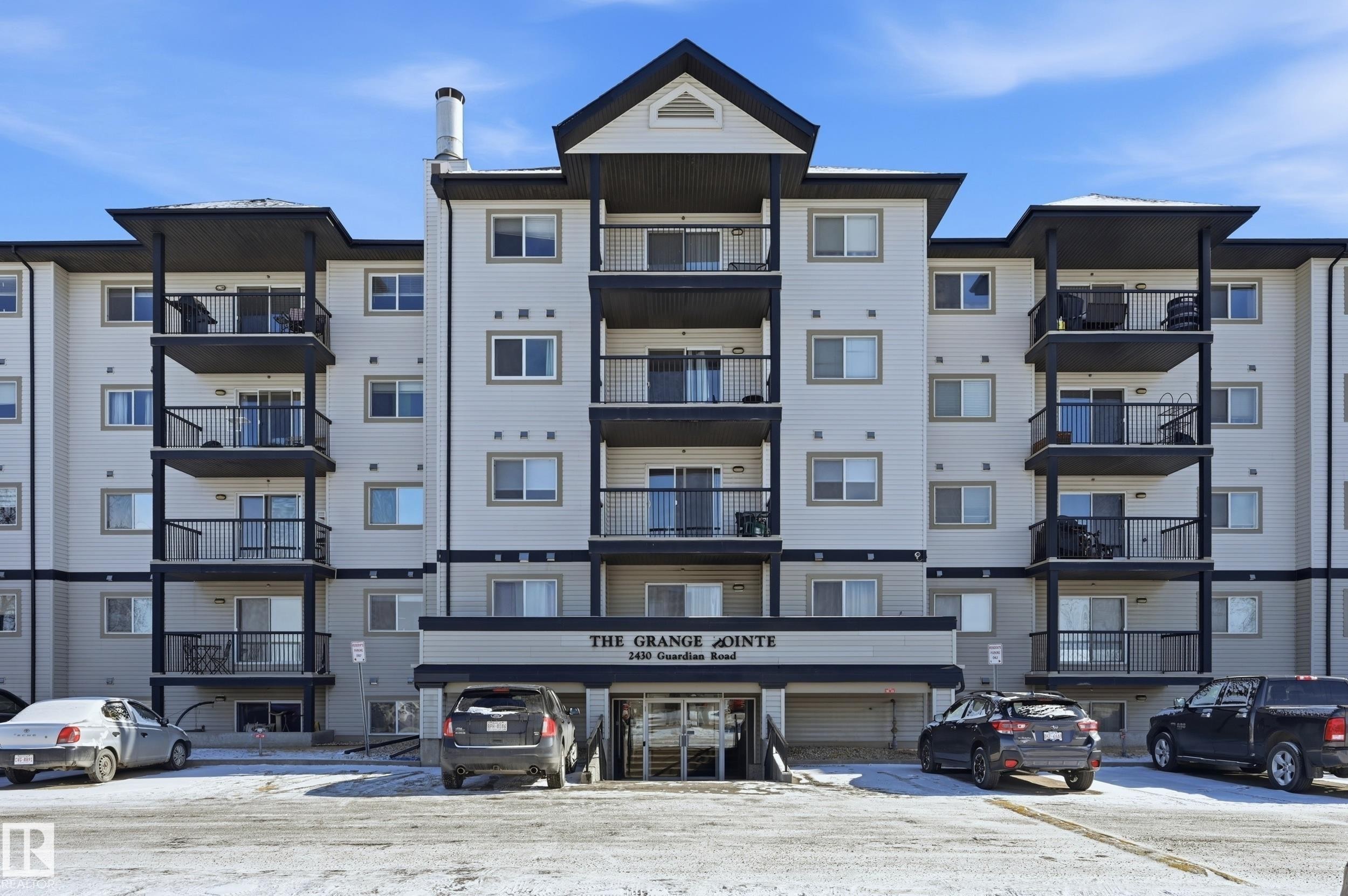 The property features a multi-story building with light-colored siding and dark accents, including balconies with black railings - 314 2430 Guardian Road, Edmonton, AB - Outdoor With Balcony With Facade