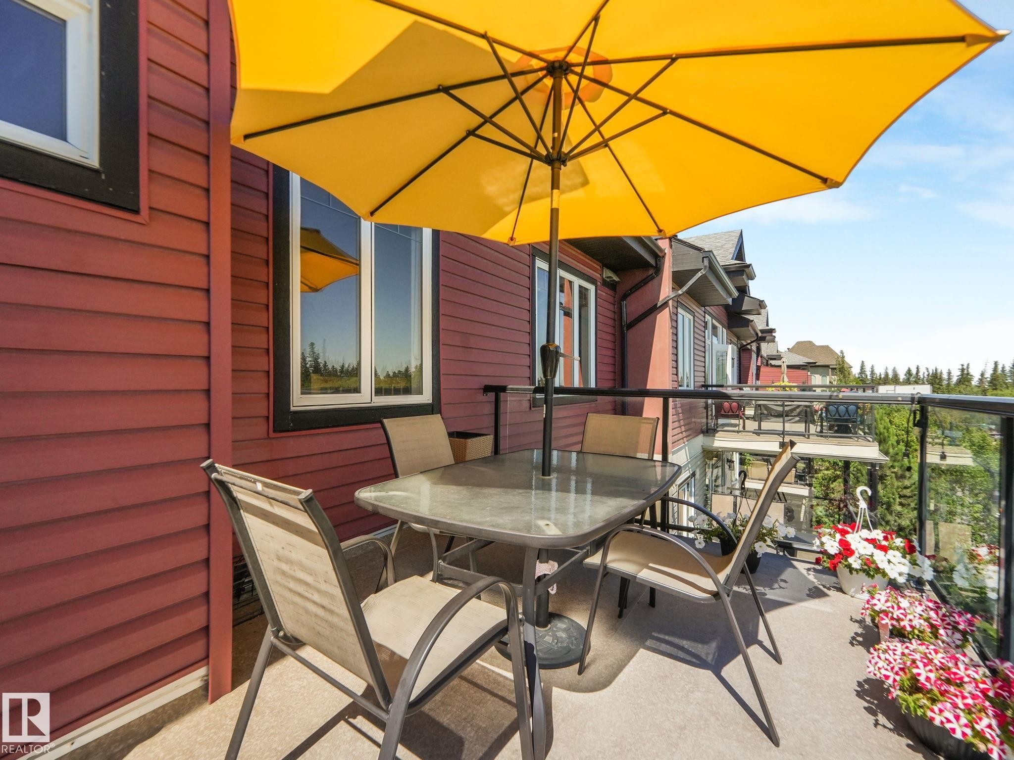 The property features a balcony with a glass railing and red siding - 412 12408 15 Avenue, Edmonton, AB - Outdoor With Deck Patio Veranda With Exterior