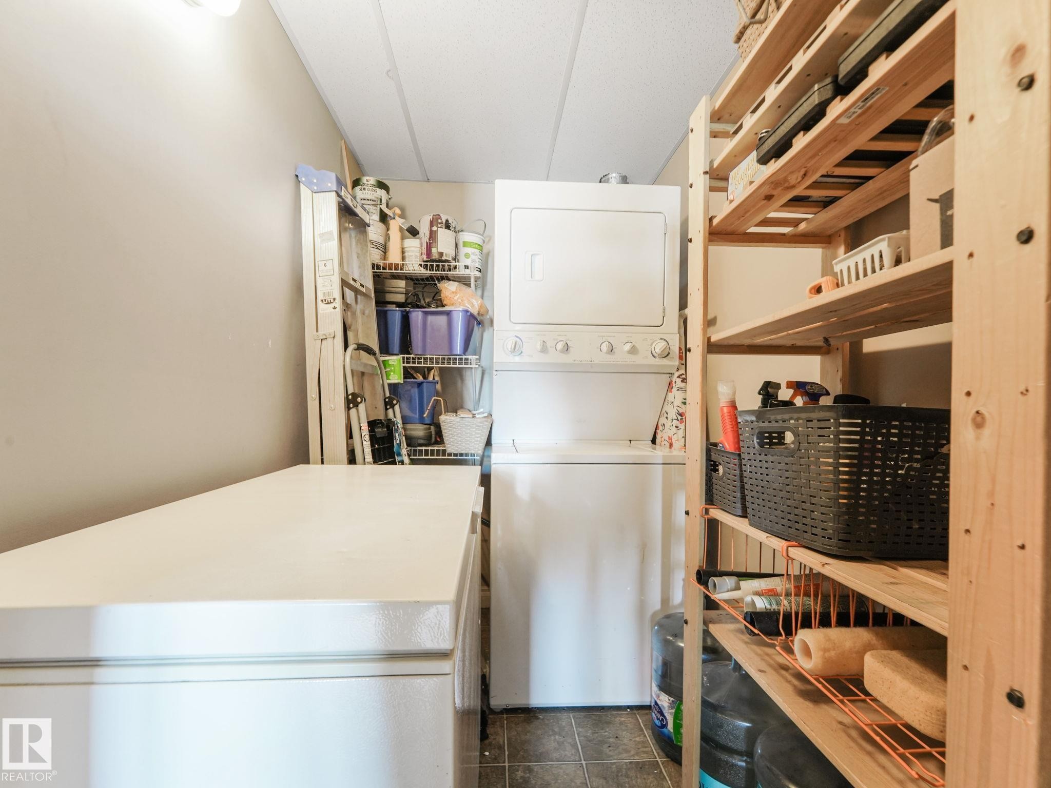 Laundry area featuring a stacked washer and dryer, tile flooring, and wood shelving - 412 12408 15 Avenue, Edmonton, AB - Indoor Photo Showing Laundry Room