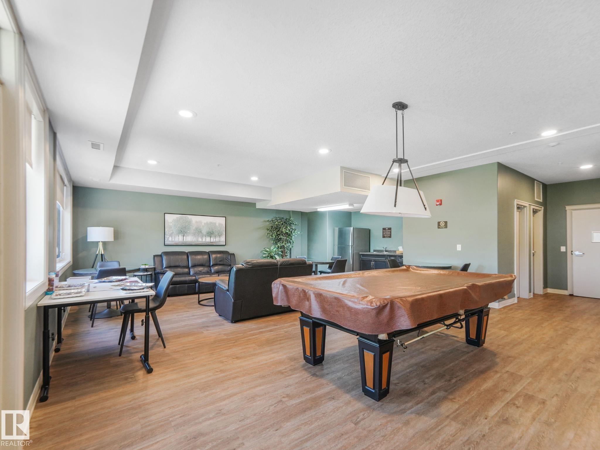 This spacious room features light wood-style flooring, ample natural light from several windows, and recessed lighting - 412 12408 15 Avenue, Edmonton, AB - Indoor Photo Showing Other Room
