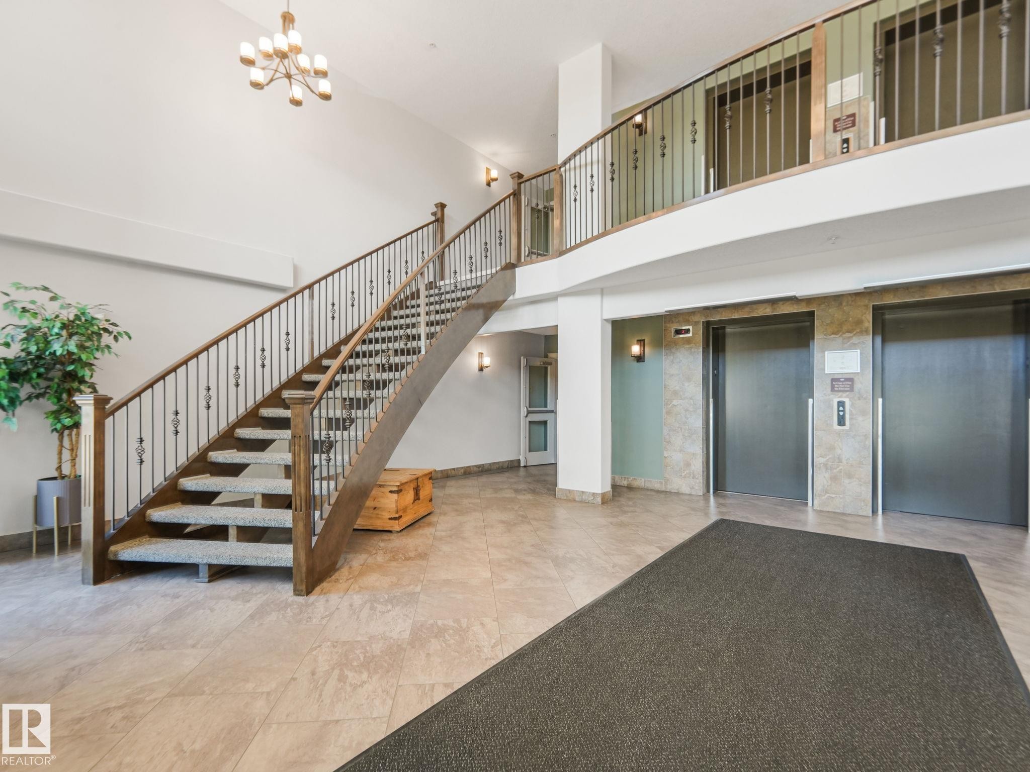 Spacious lobby featuring a grand staircase with ornate railings, tiled flooring, and dual elevators for convenient access - 412 12408 15 Avenue, Edmonton, AB - Indoor Photo Showing Other Room