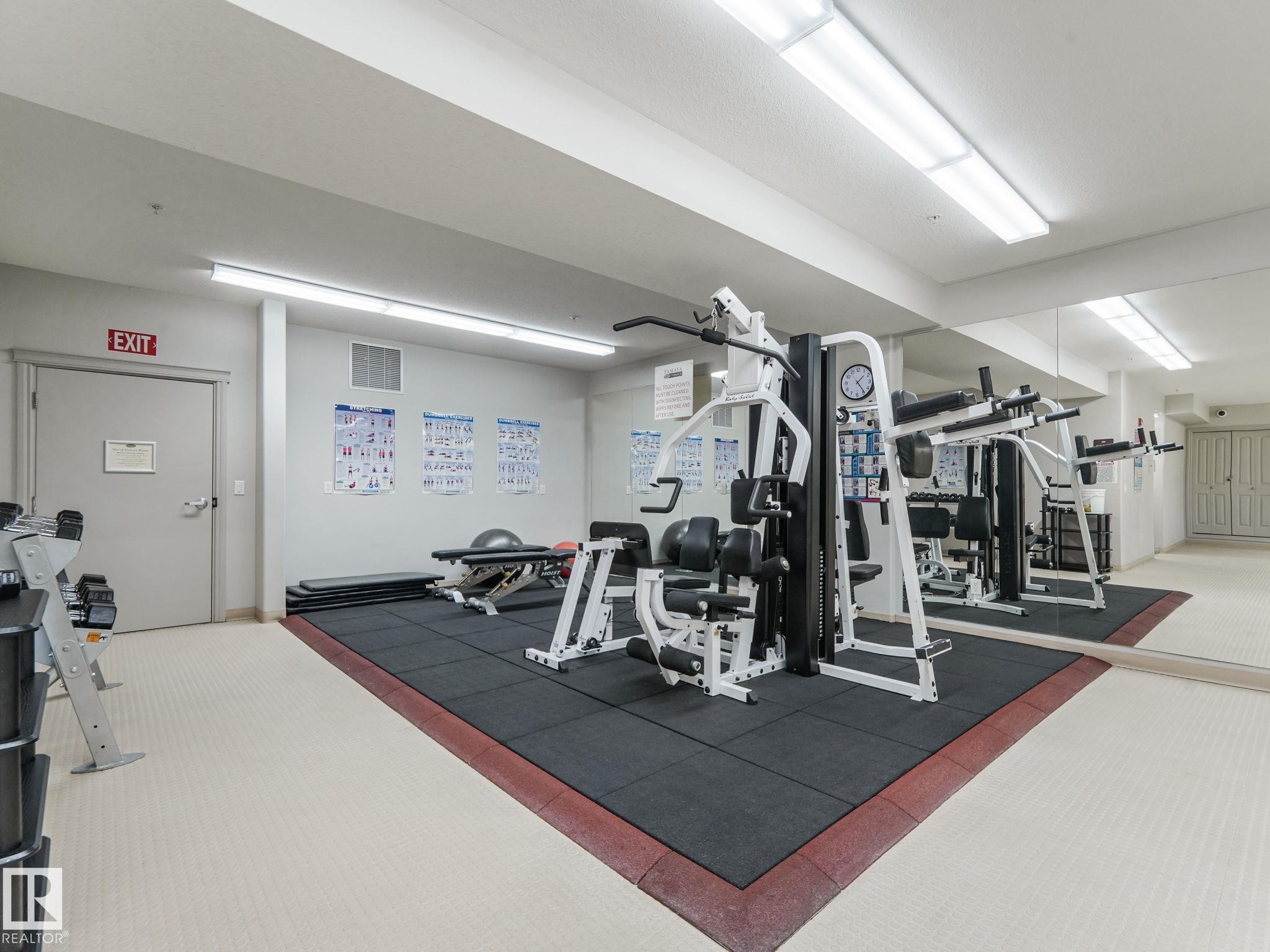 Well-equipped fitness room featuring a multi-station gym, weight bench, exercise mat flooring, and mirrored wall - 412 12408 15 Avenue, Edmonton, AB - Indoor Photo Showing Gym Room