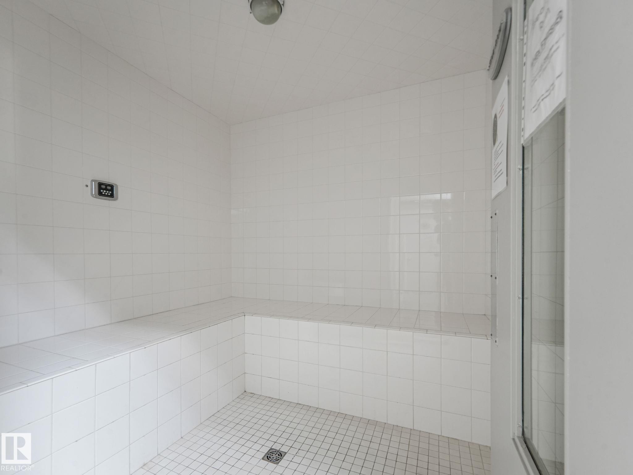 The property features a tiled room with built-in bench seating and a tiled floor with a drain - 412 12408 15 Avenue, Edmonton, AB - Indoor Photo Showing Bathroom