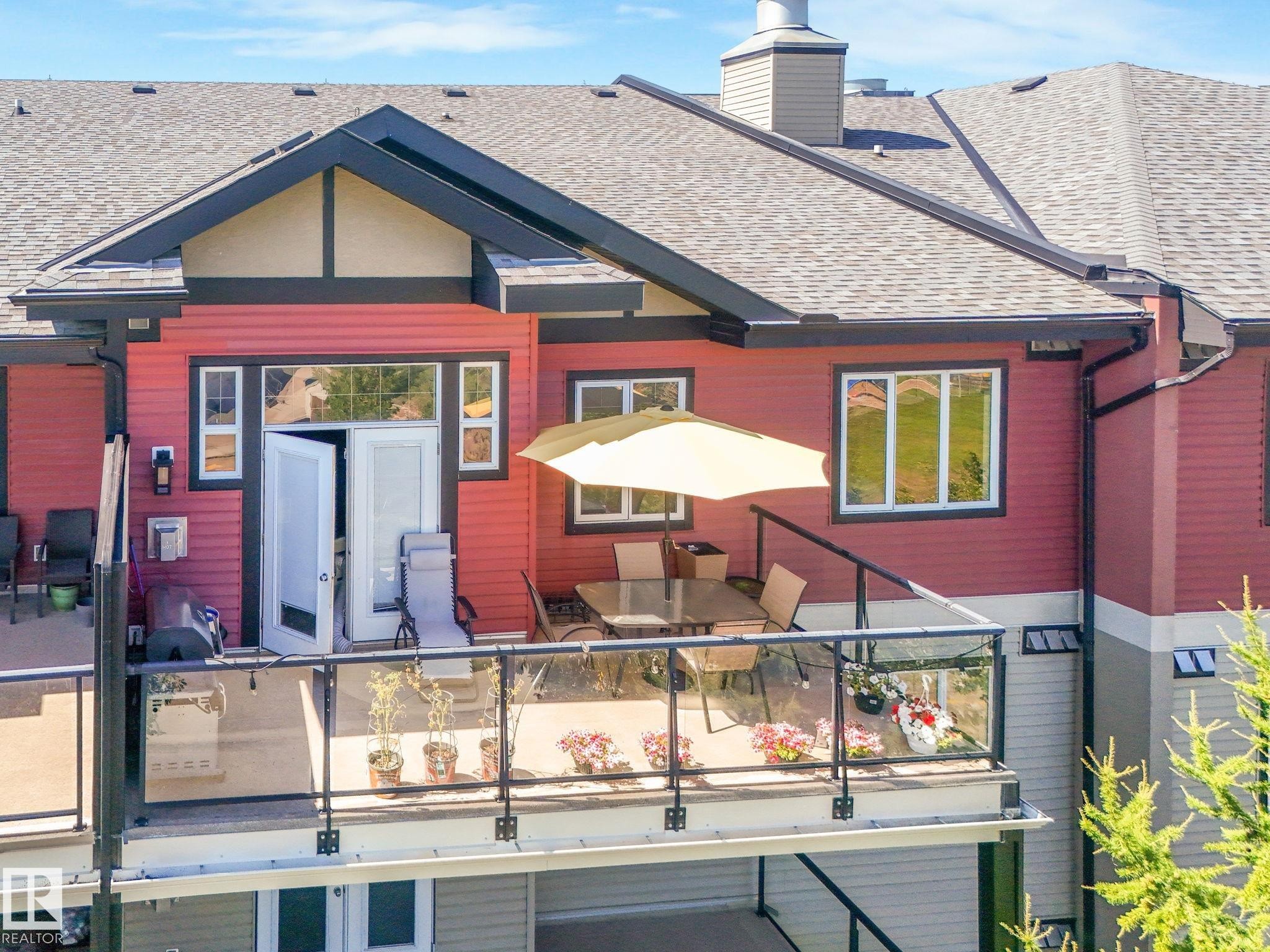 The property features a spacious deck with glass railings, a patio umbrella, and direct access to the interior through double doors - 412 12408 15 Avenue, Edmonton, AB - Outdoor