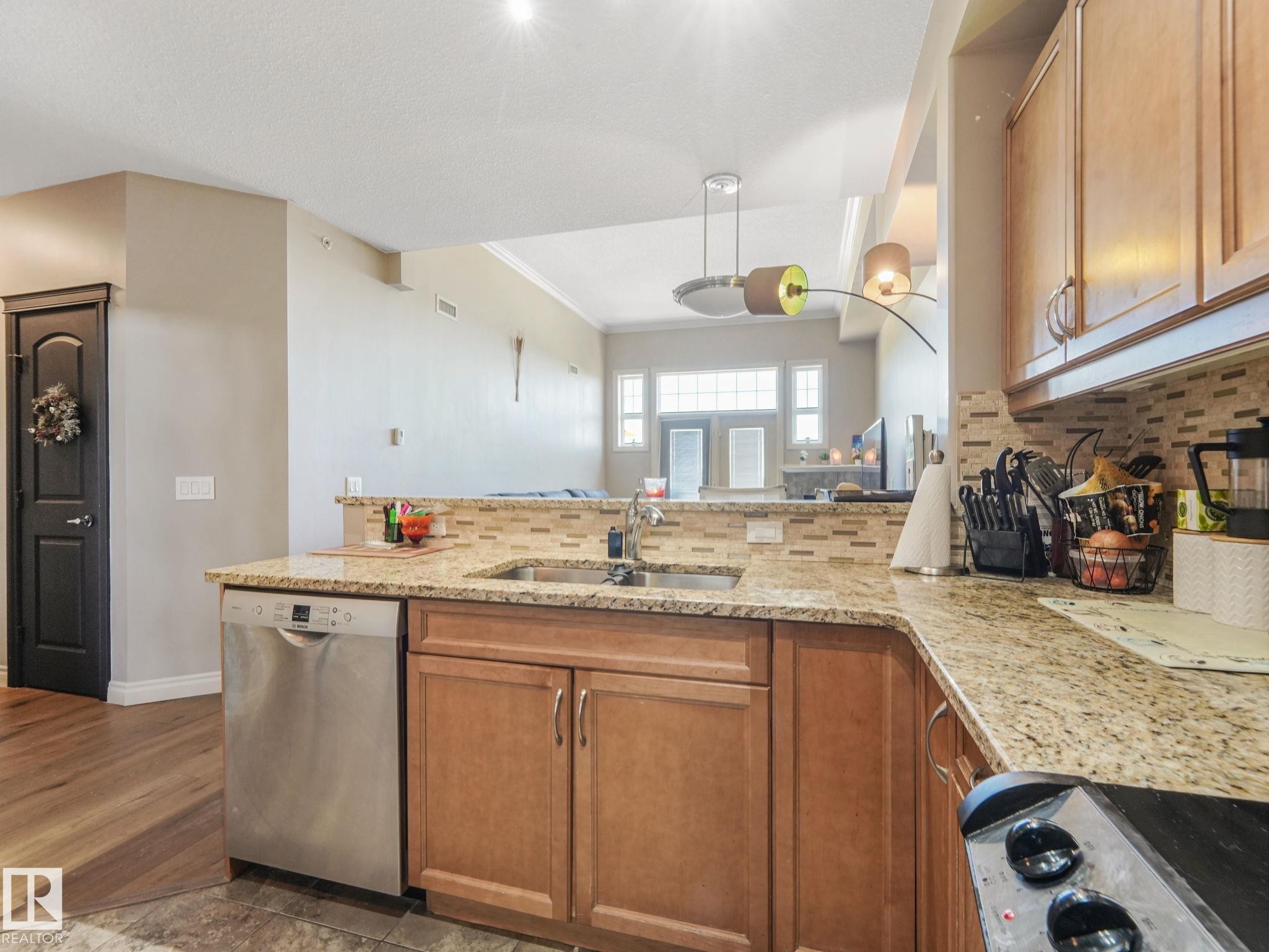 The kitchen features granite countertops, a tiled backsplash, and wooden cabinetry - 412 12408 15 Avenue, Edmonton, AB - Indoor Photo Showing Kitchen With Double Sink
