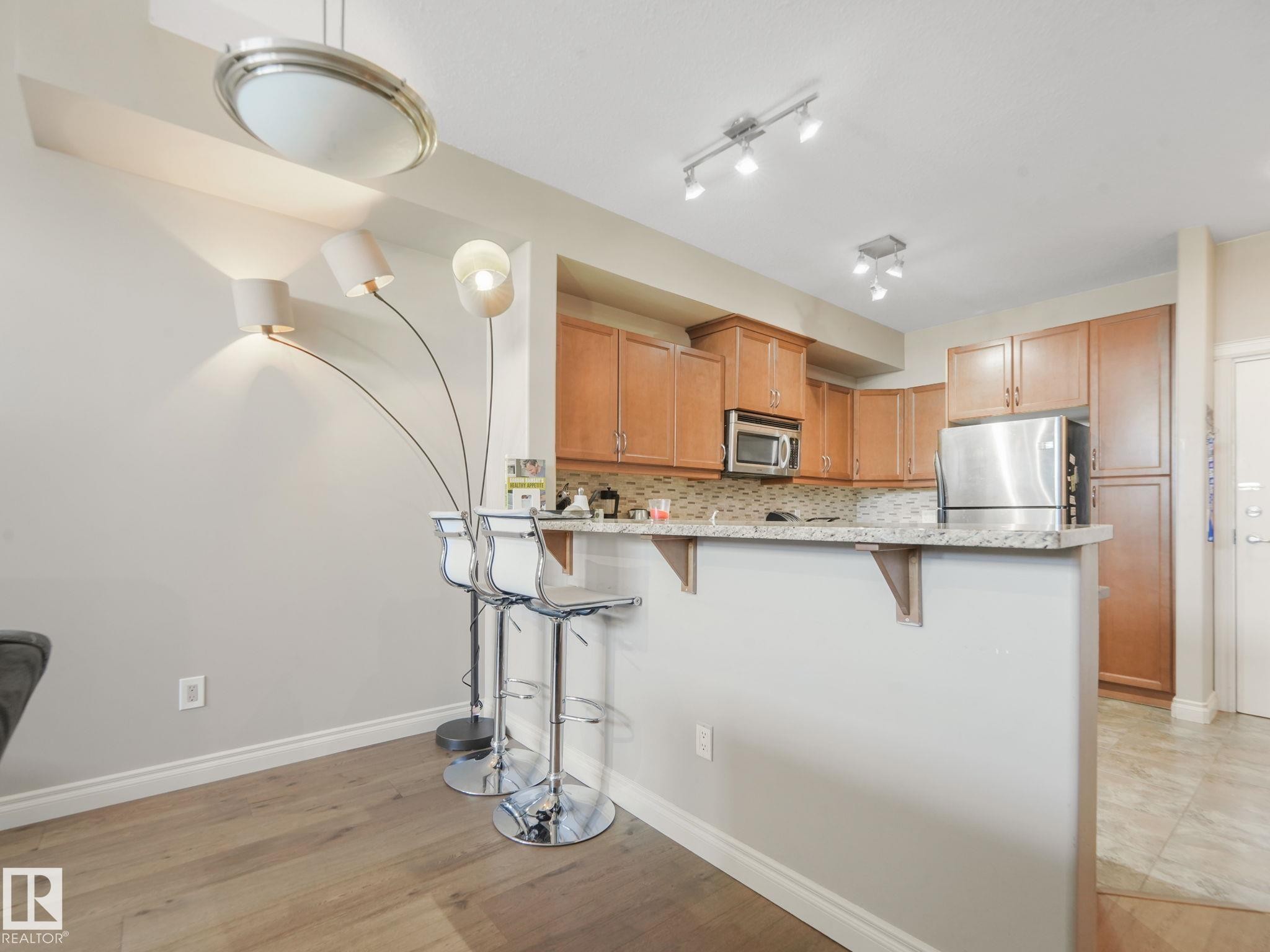 The property features an open-concept living area with wood flooring and light-colored walls - 412 12408 15 Avenue, Edmonton, AB - Indoor Photo Showing Kitchen