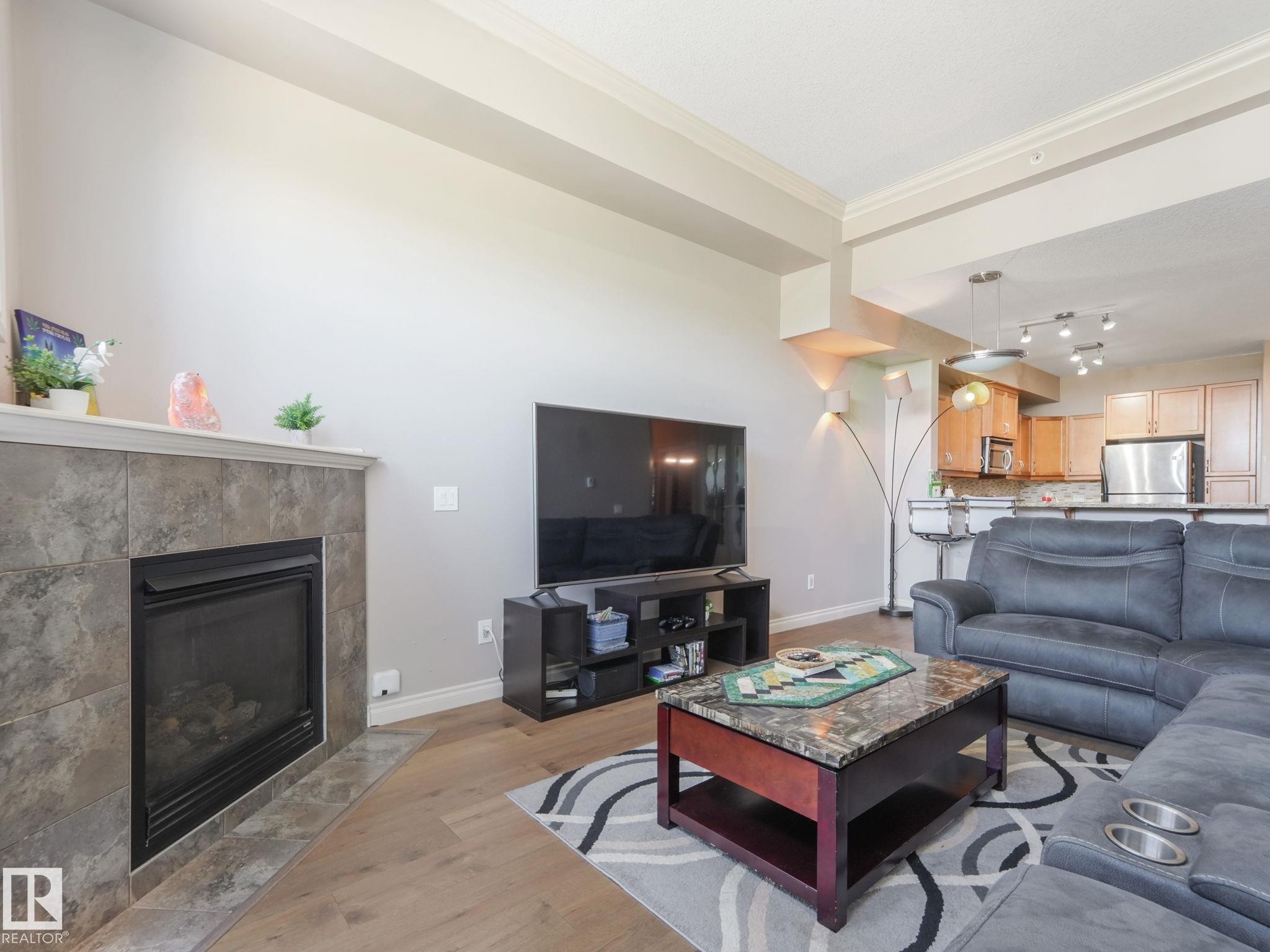 Living area featuring hardwood flooring, a tiled fireplace with a mantel, and crown molding - 412 12408 15 Avenue, Edmonton, AB - Indoor Photo Showing Living Room With Fireplace