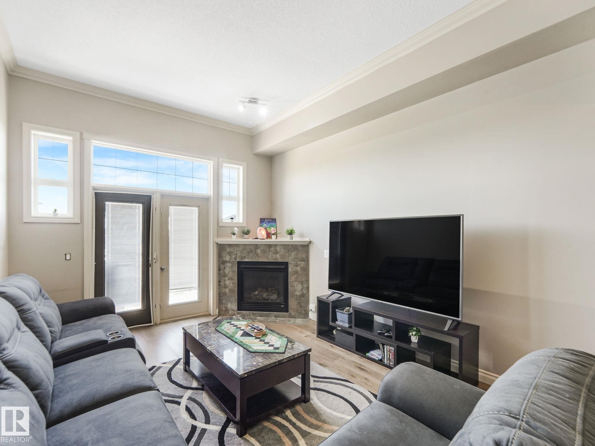Living area featuring a corner fireplace with a tiled surround, two glass-paned doors, and multiple windows providing natural light - 412 12408 15 Avenue, Edmonton, AB - Indoor Photo Showing Living Room With Fireplace