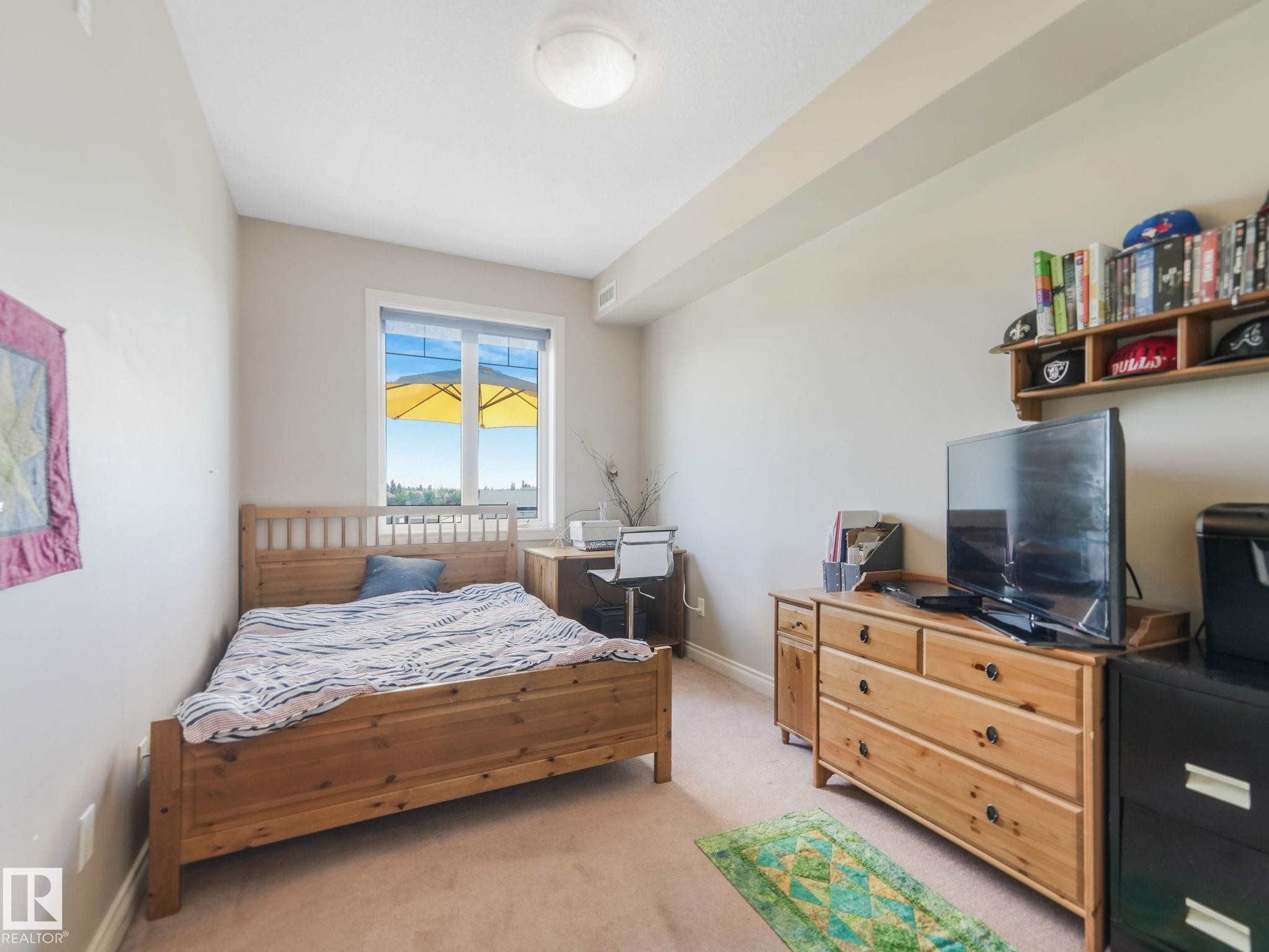 This room features a window providing natural light, carpeted flooring, and a ceiling light fixture - 412 12408 15 Avenue, Edmonton, AB - Indoor Photo Showing Bedroom