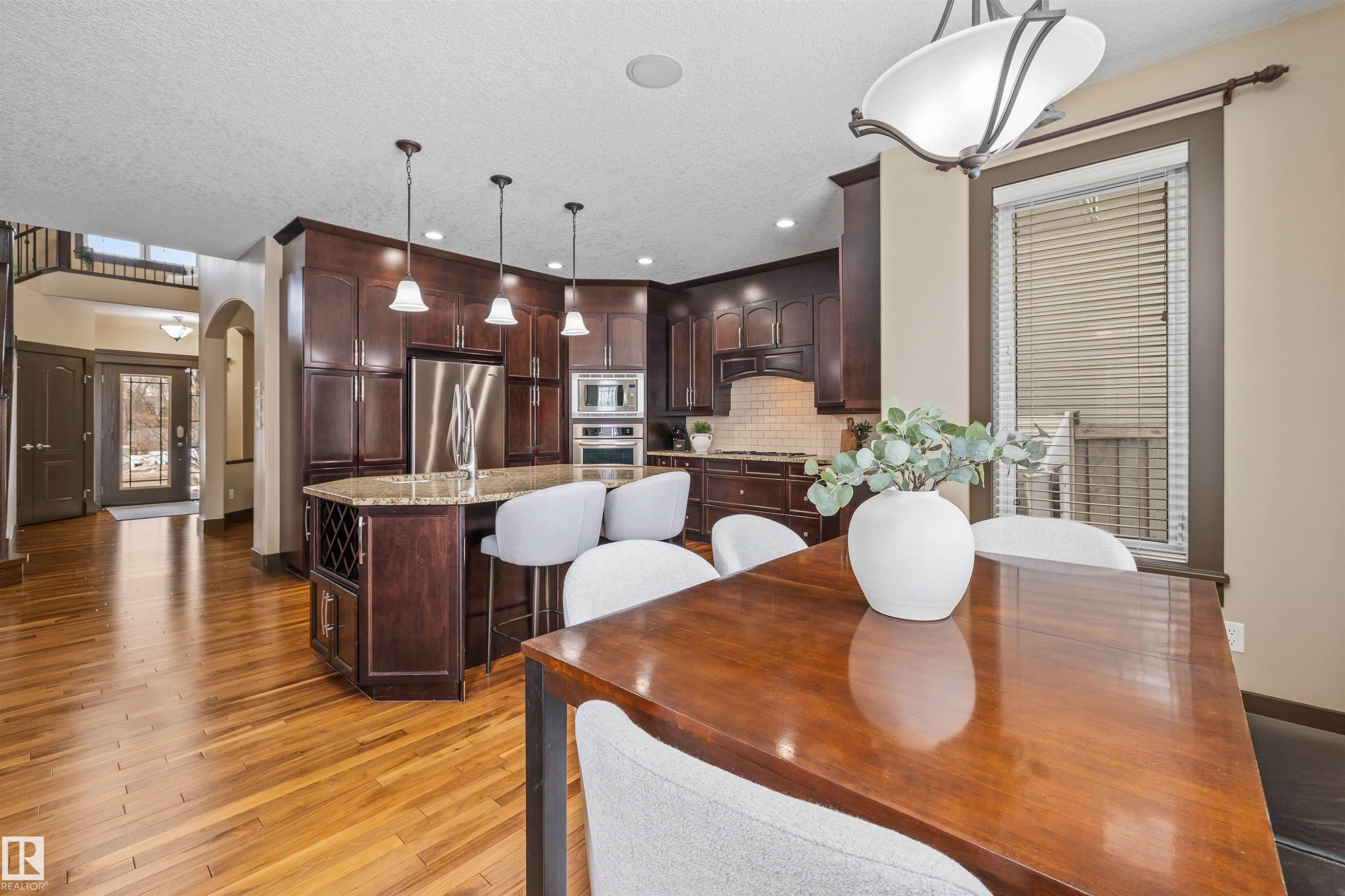 The property features a spacious open-concept kitchen and dining area with hardwood flooring, dark wood cabinetry, a large kitchen island with seating, and stainless steel appliances - 1014 Hope Road, Edmonton, AB - Indoor Photo Showing Dining Room