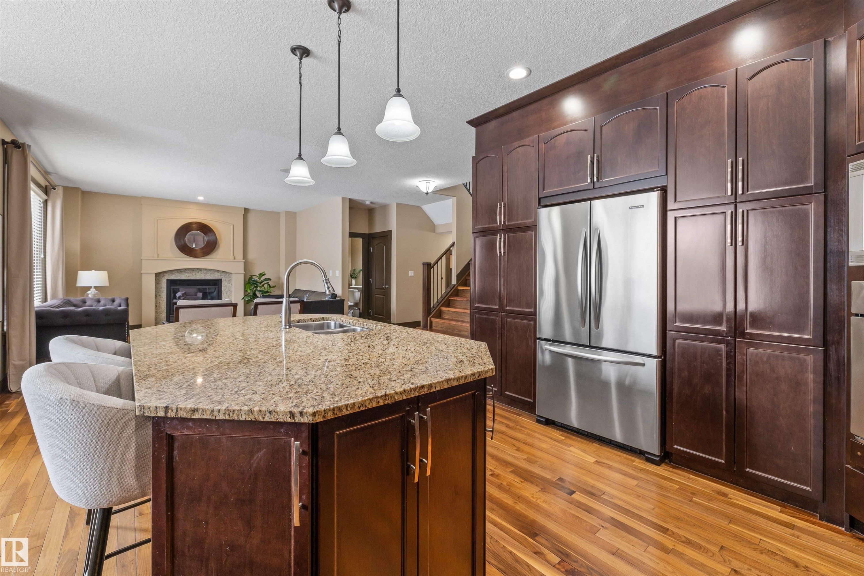 The kitchen features a large island with a granite countertop and an undermount sink, dark wood cabinetry, and a stainless steel refrigerator - 1014 Hope Road, Edmonton, AB - Indoor Photo Showing Kitchen With Double Sink With Upgraded Kitchen