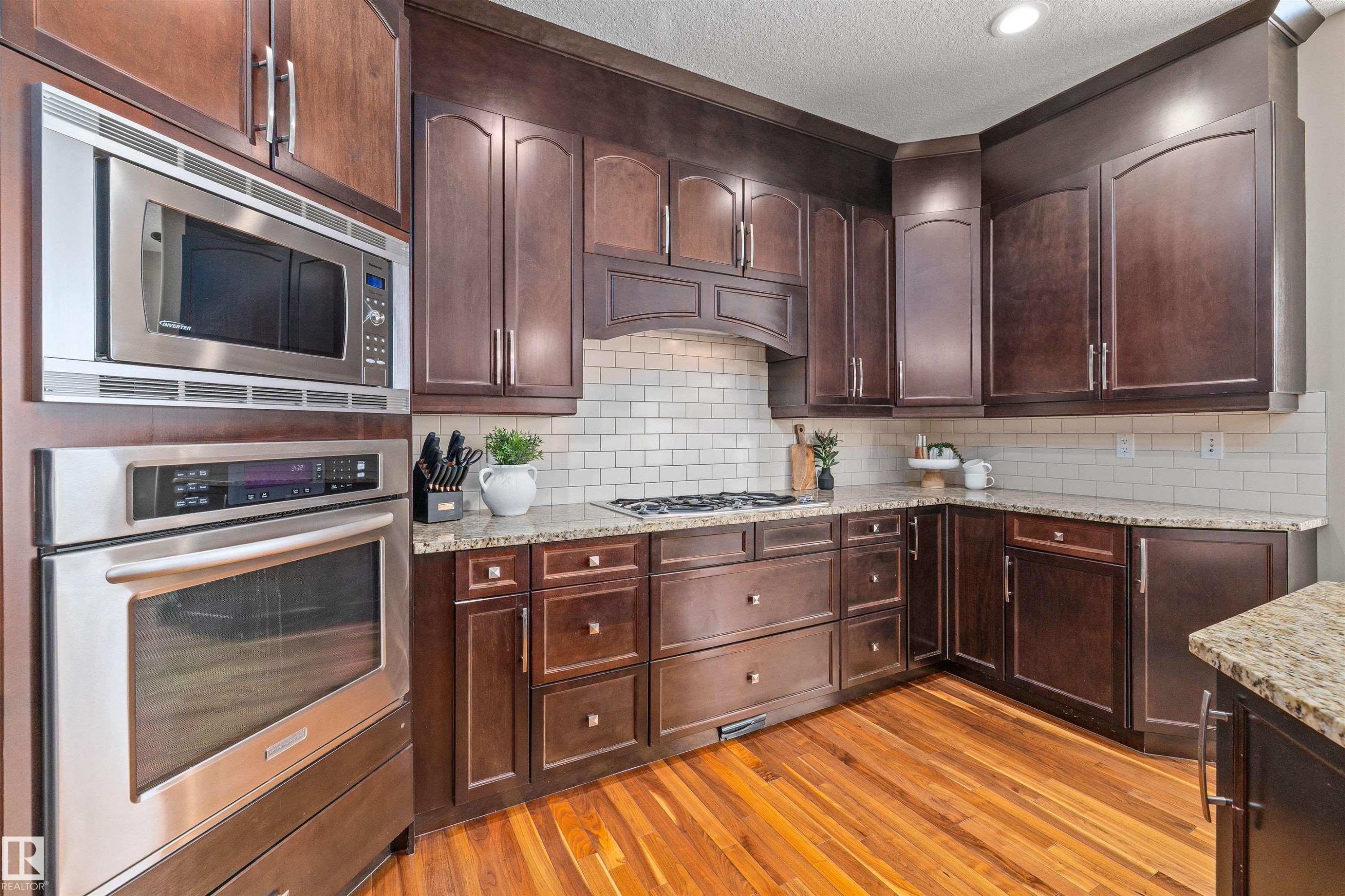 The kitchen features rich wood cabinetry, granite countertops, a subway tile backsplash, and stainless steel appliances including a built-in oven and microwave - 1014 Hope Road, Edmonton, AB - Indoor Photo Showing Kitchen