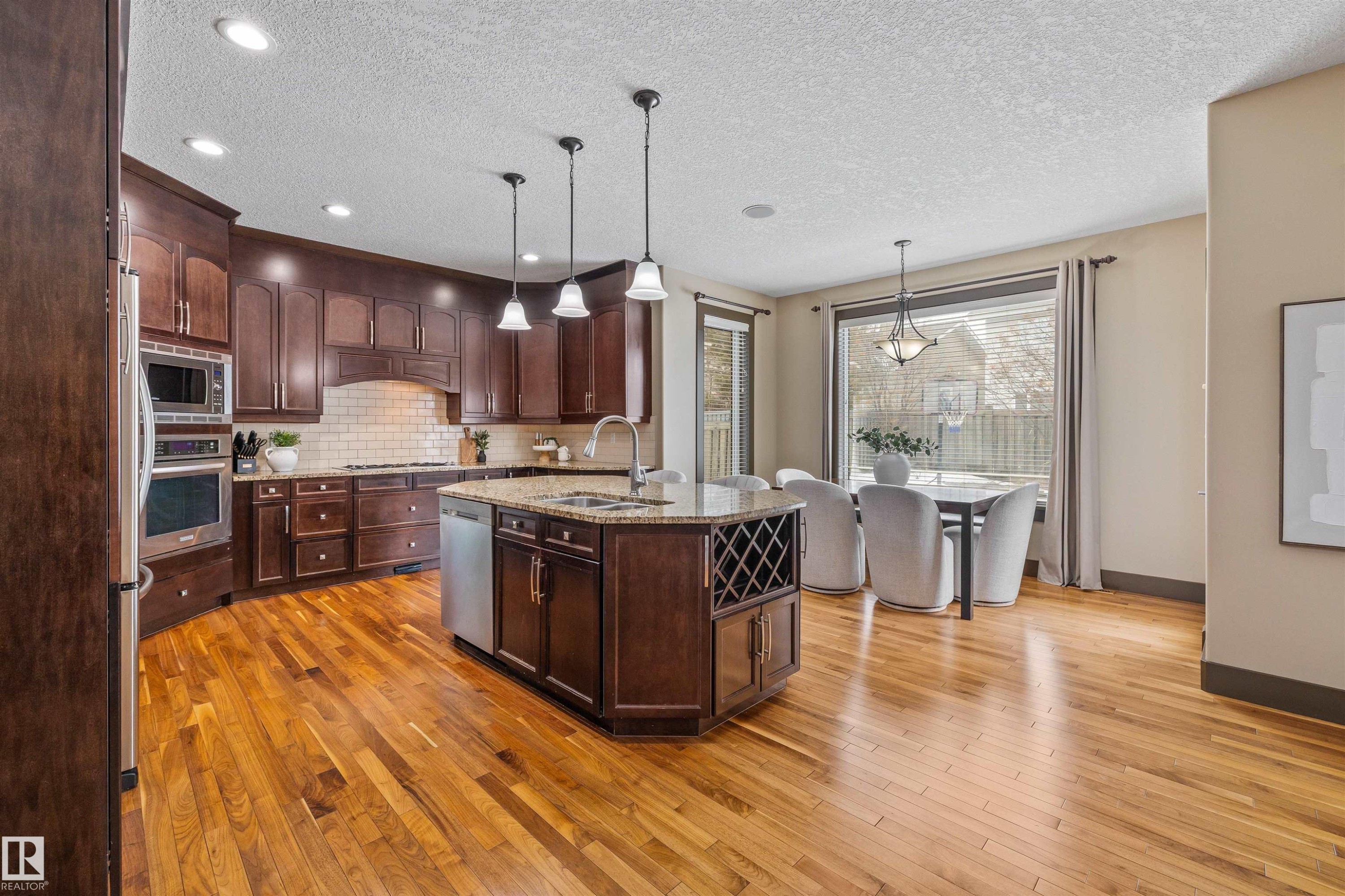 Kitchen featuring hardwood floors, dark wood cabinetry, stainless steel appliances, and a central island with a granite countertop - 1014 Hope Road, Edmonton, AB - Indoor Photo Showing Kitchen With Upgraded Kitchen