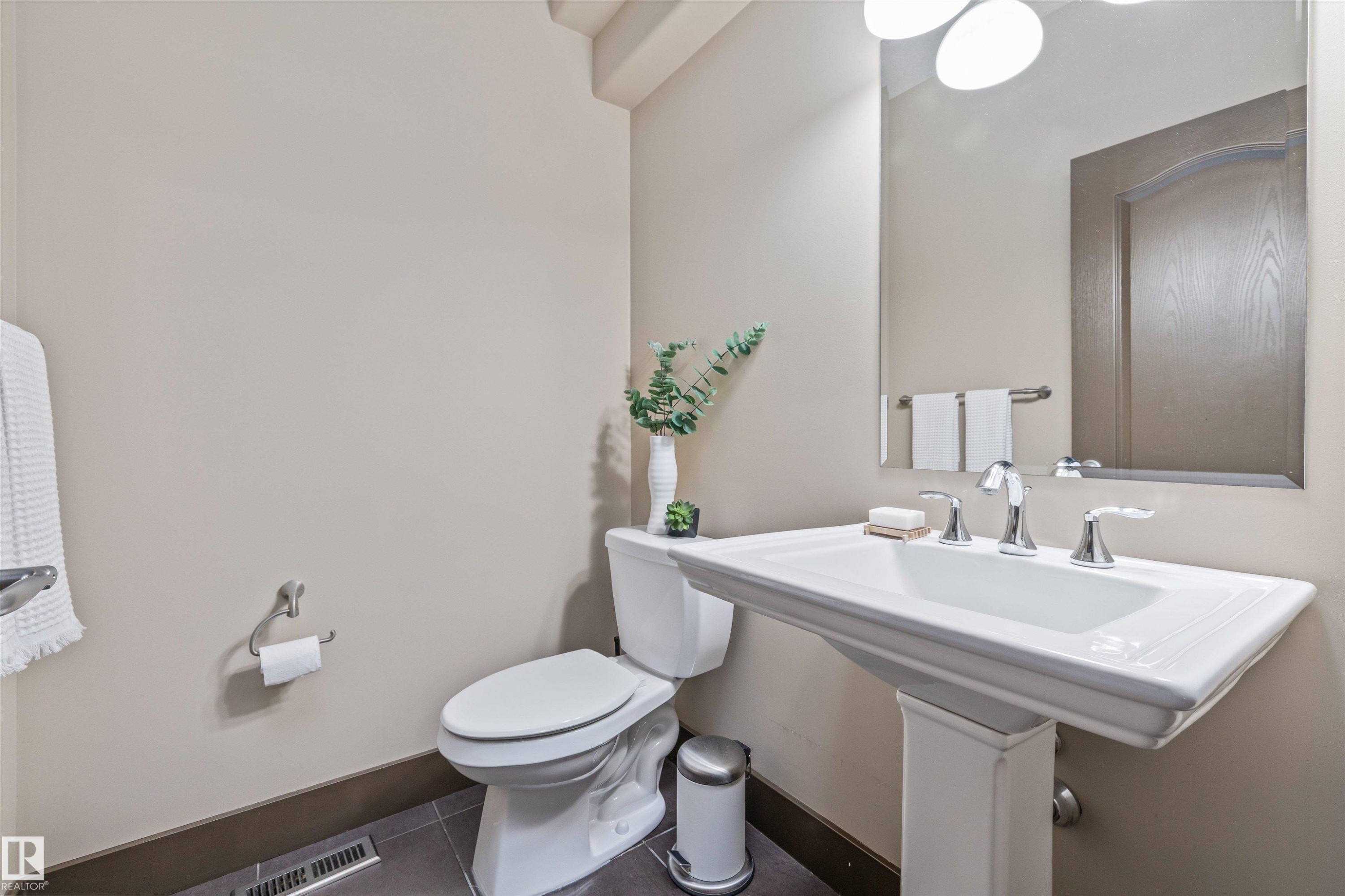This bathroom features a pedestal sink with chrome fixtures, a toilet, a wall-mounted mirror, and tiled flooring - 1014 Hope Road, Edmonton, AB - Indoor Photo Showing Bathroom