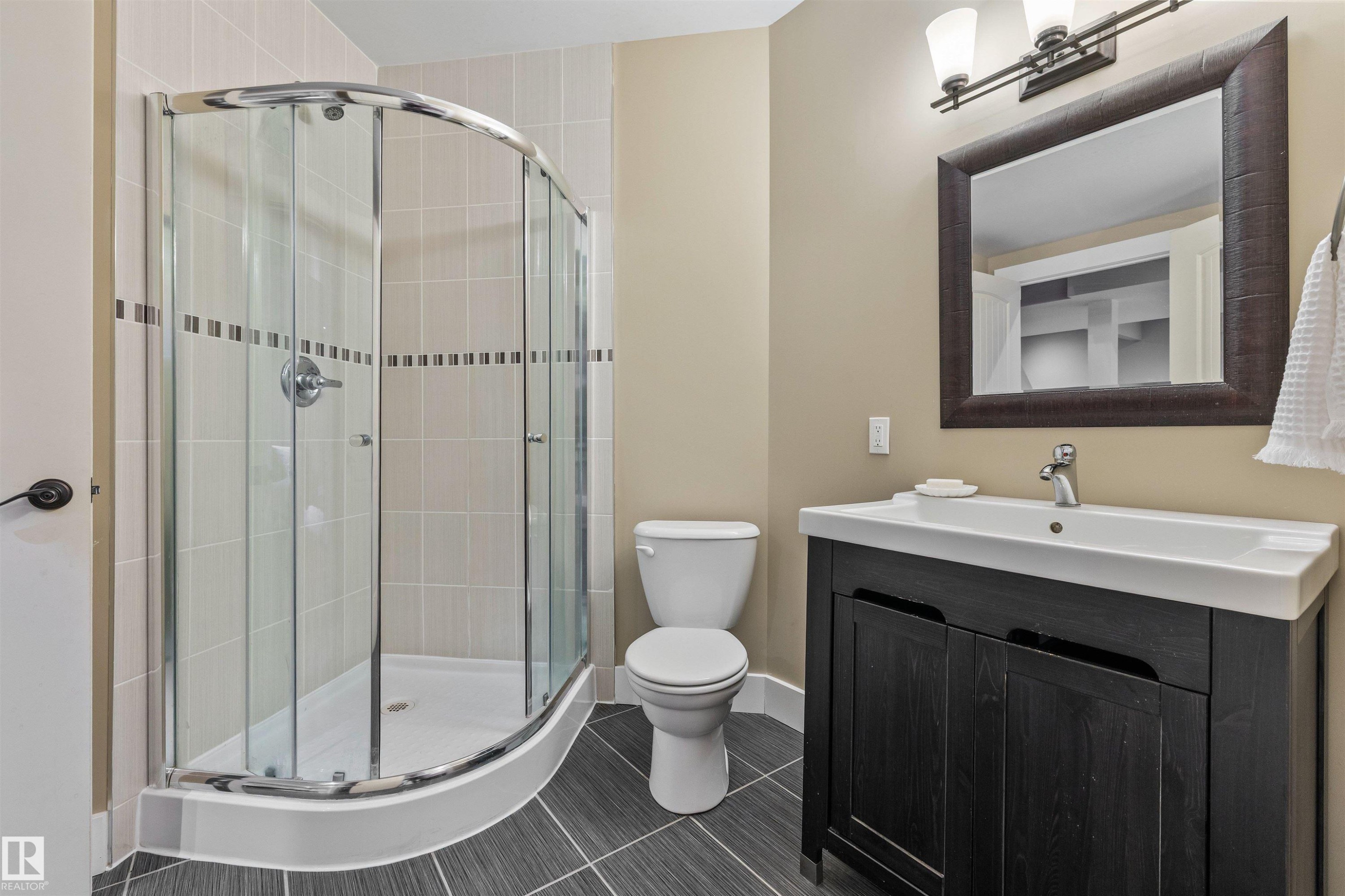 The bathroom features a curved glass shower enclosure, a toilet, a vanity with a dark wood cabinet, and a framed mirror above the vanity - 1014 Hope Road, Edmonton, AB - Indoor Photo Showing Bathroom