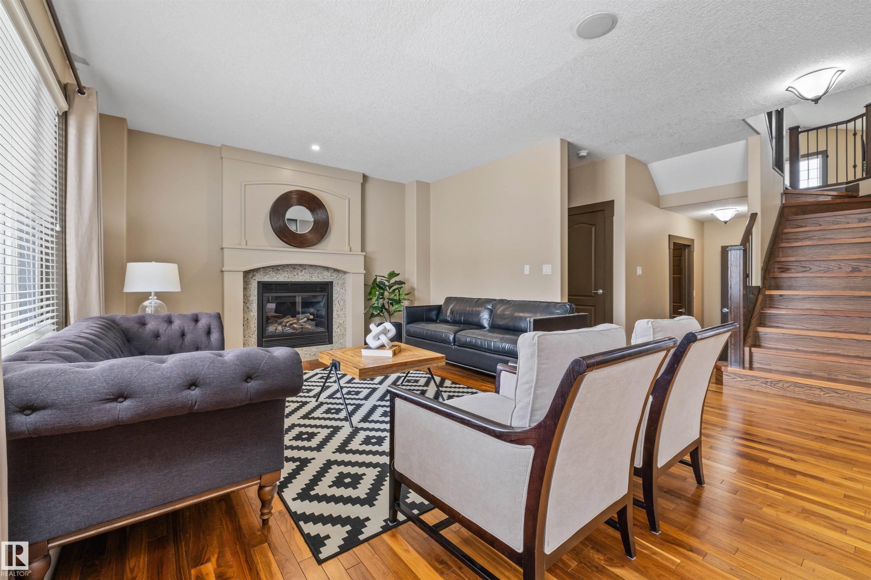 Living area featuring hardwood floors, a fireplace with a stone surround, and a wooden staircase with a dark banister - 1014 Hope Road, Edmonton, AB - Indoor Photo Showing Living Room With Fireplace