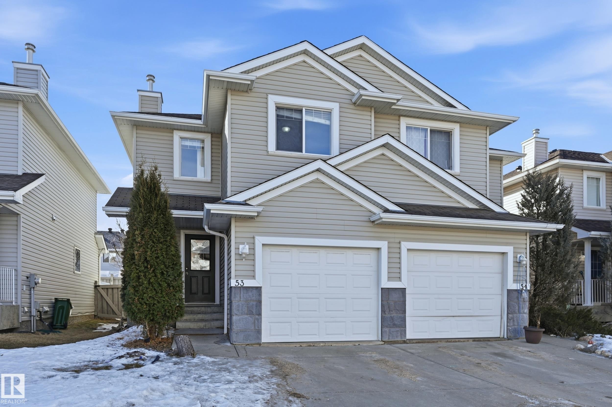 This property features a two-story exterior with light-colored siding, a dark front door, and a two-car garage - 53 287 Macewan Road, Edmonton, AB - Outdoor With Facade