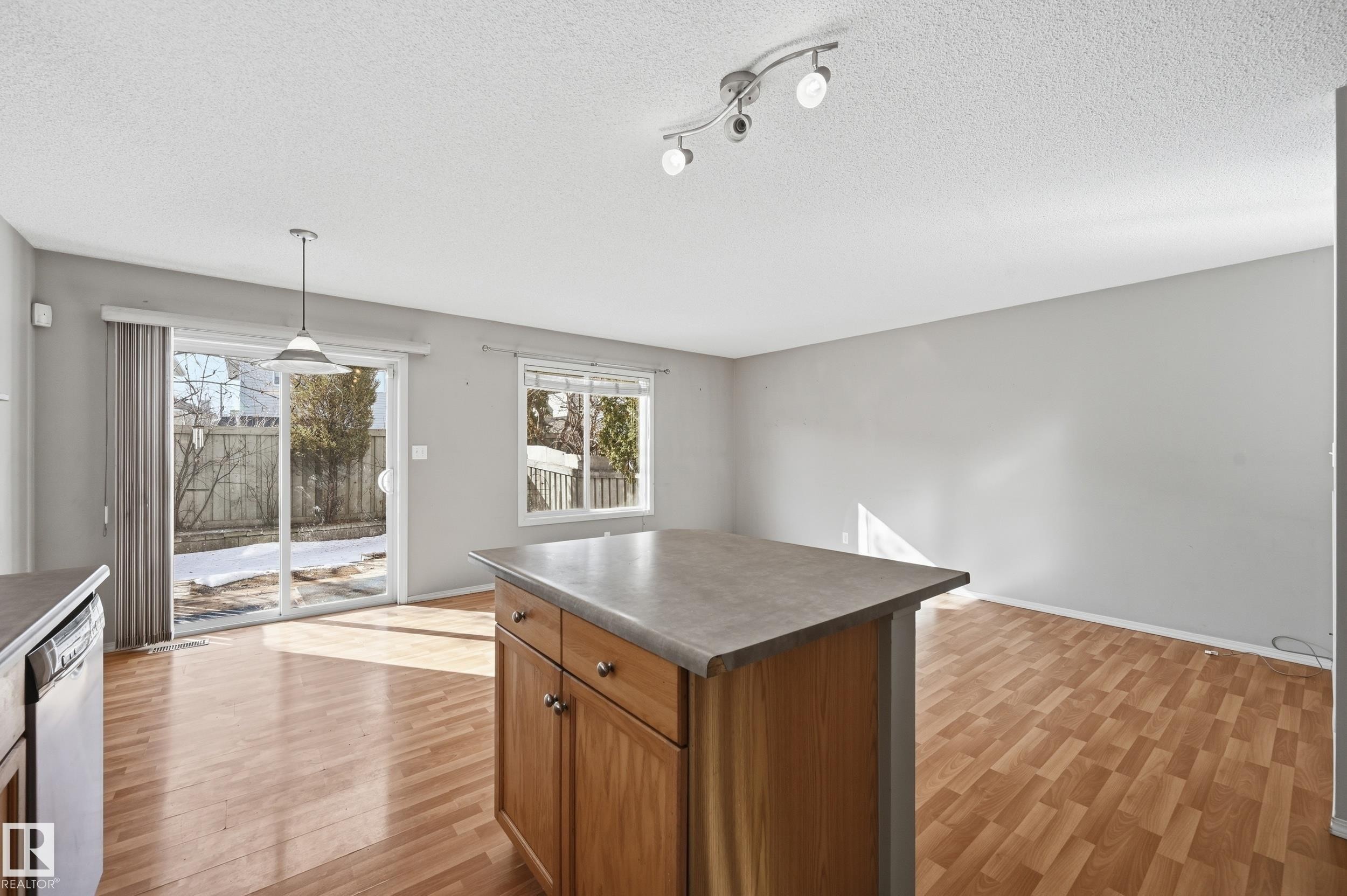 This bright living area features light wood flooring, a central island with wood cabinetry, and track lighting - 53 287 Macewan Road, Edmonton, AB - Indoor Photo Showing Other Room