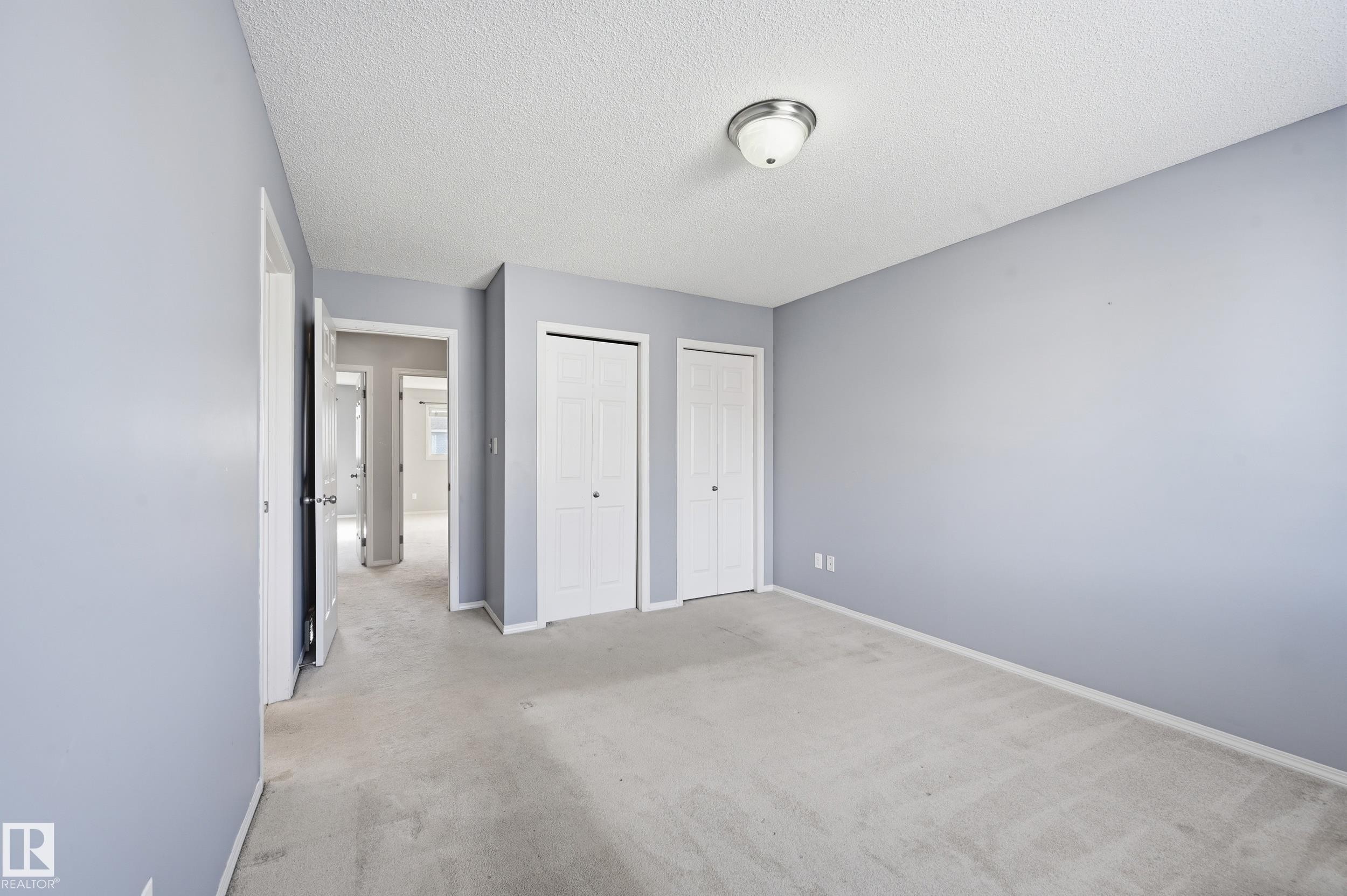 Room with light blue walls, light-colored carpet, a ceiling-mounted light fixture, and two white bi-fold closet doors - 53 287 Macewan Road, Edmonton, AB - Indoor Photo Showing Other Room
