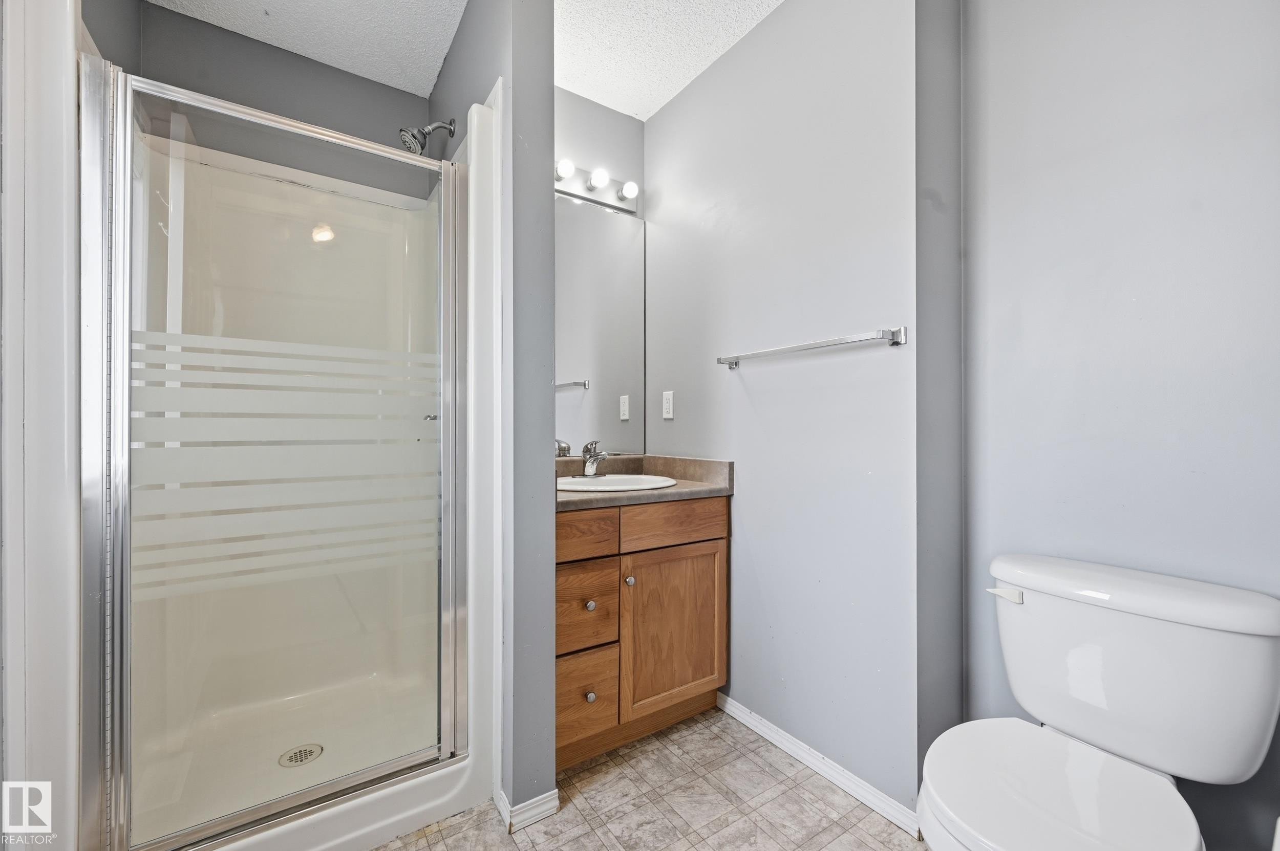 The bathroom features a glass-enclosed shower, a vanity with a sink and storage, and a toilet - 53 287 Macewan Road, Edmonton, AB - Indoor Photo Showing Bathroom