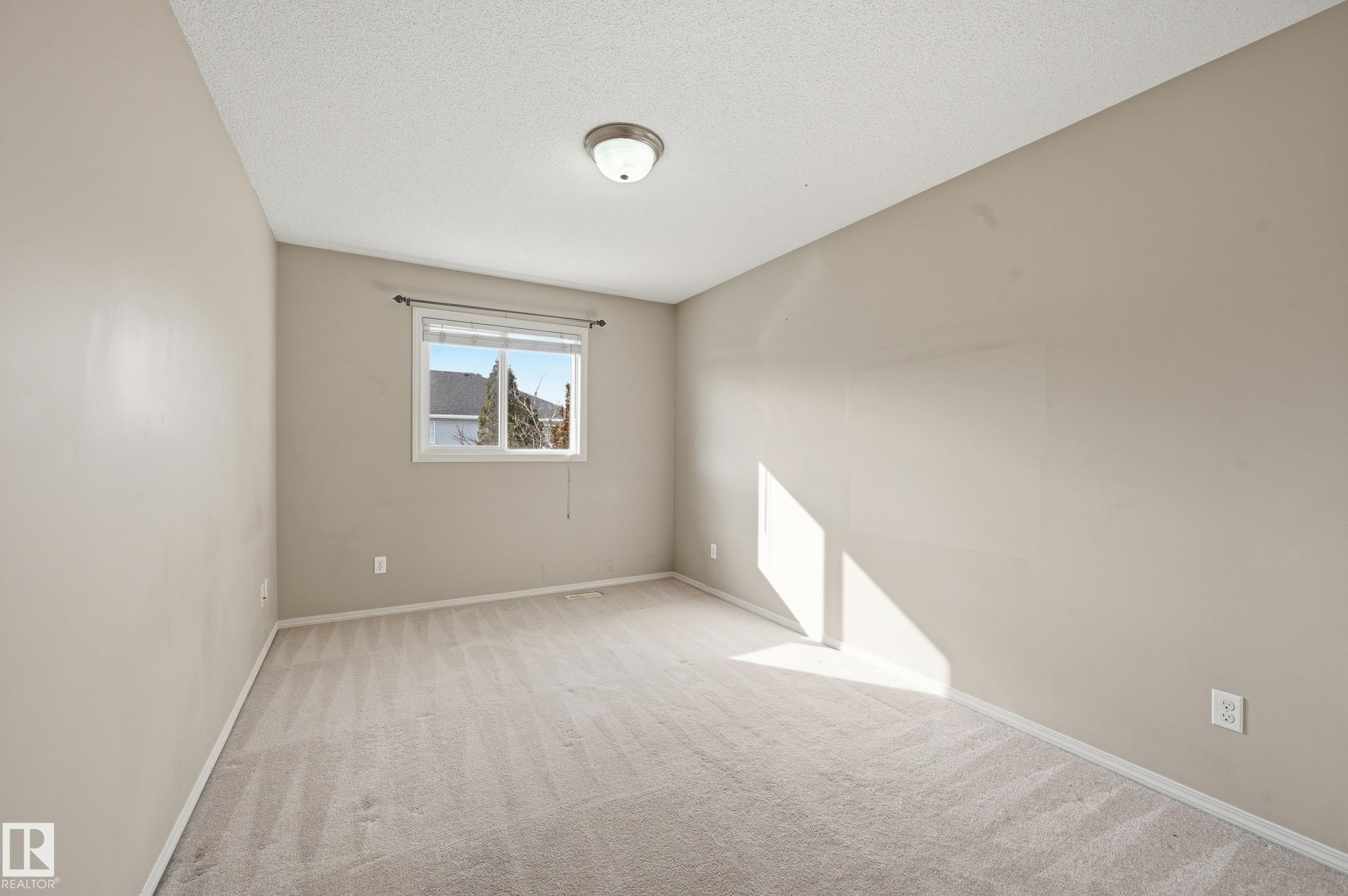This room features a neutral color palette, plush carpeting, a window providing natural light, and a ceiling-mounted light fixture - 53 287 Macewan Road, Edmonton, AB - Indoor Photo Showing Other Room