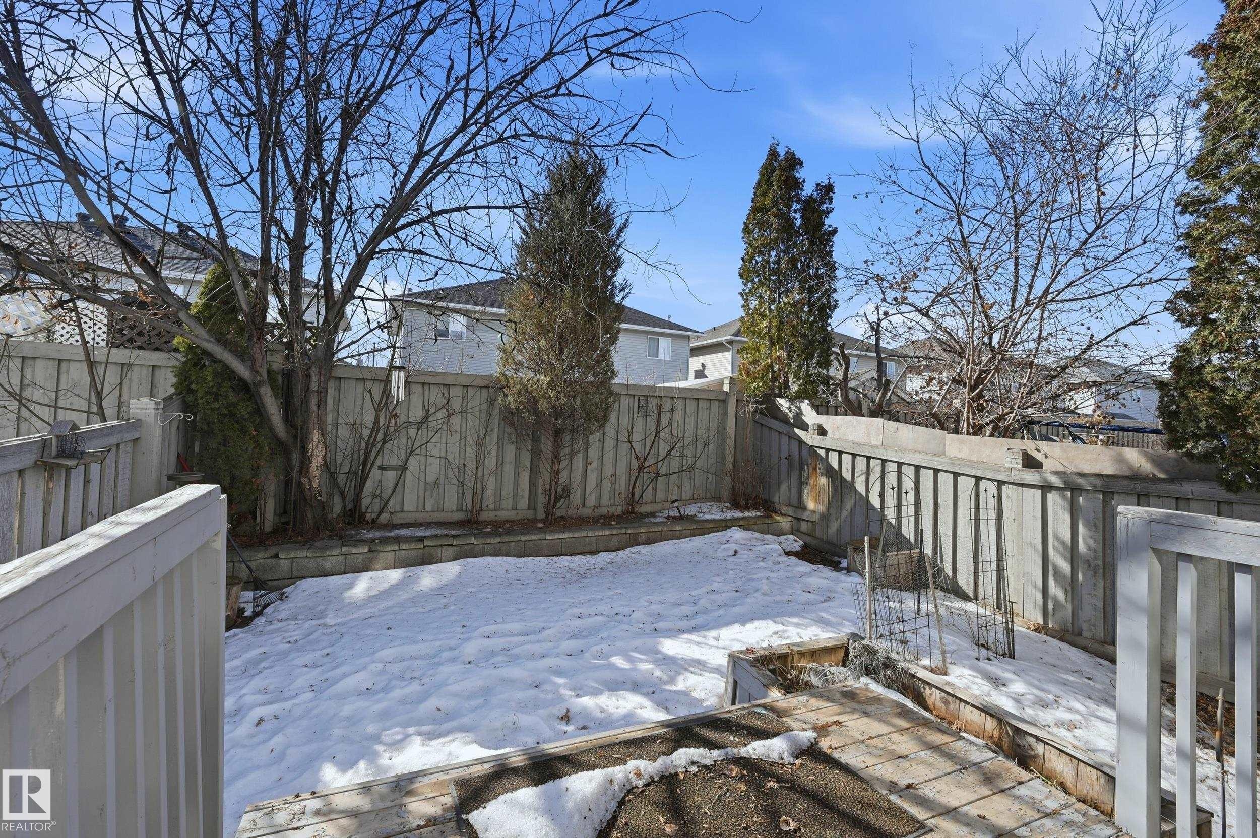 The property features a fenced backyard with mature trees and a raised garden bed - 53 287 Macewan Road, Edmonton, AB - Outdoor