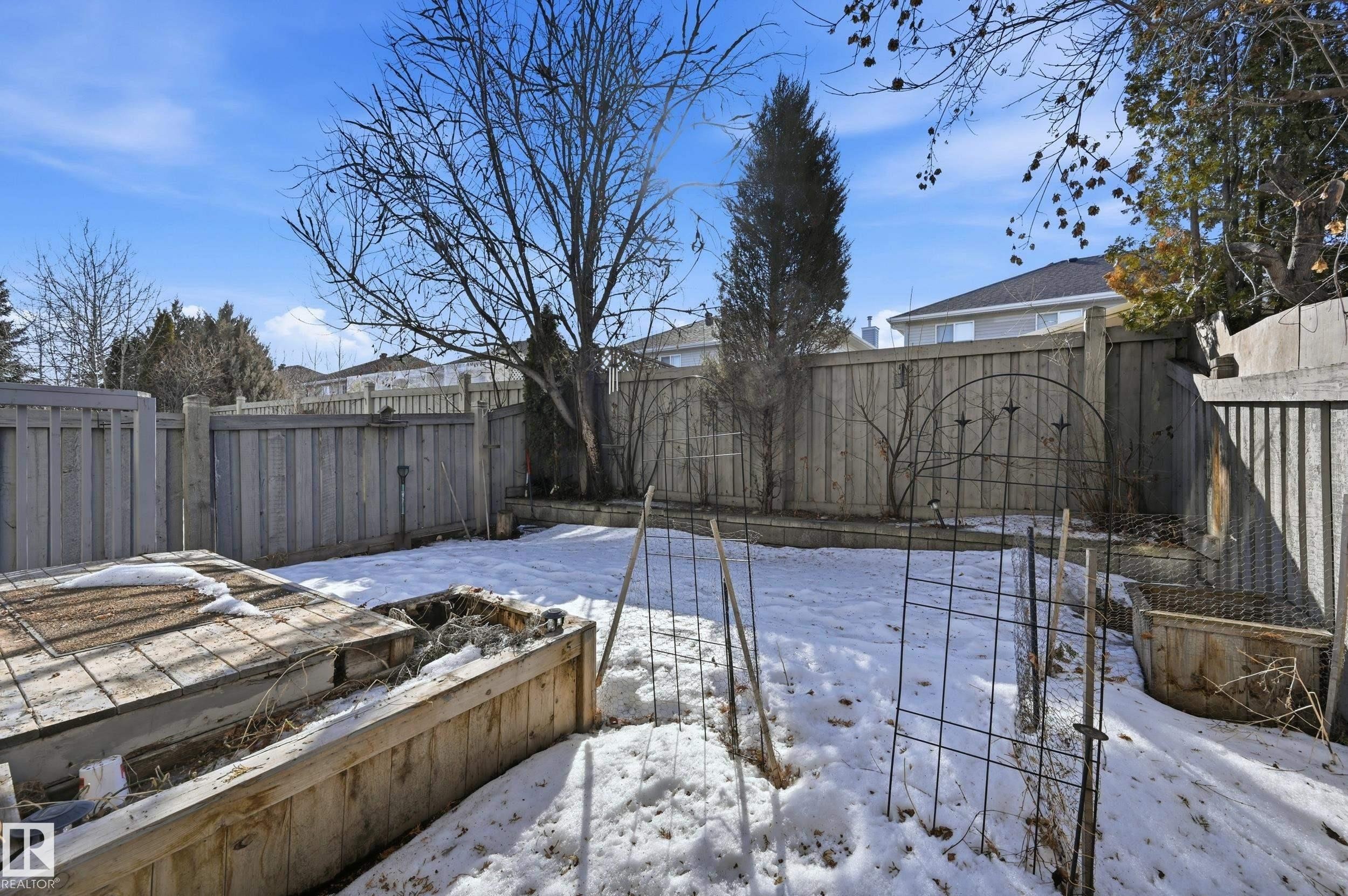The property features a fenced yard with raised garden beds and a clear blue sky overhead - 53 287 Macewan Road, Edmonton, AB - Outdoor