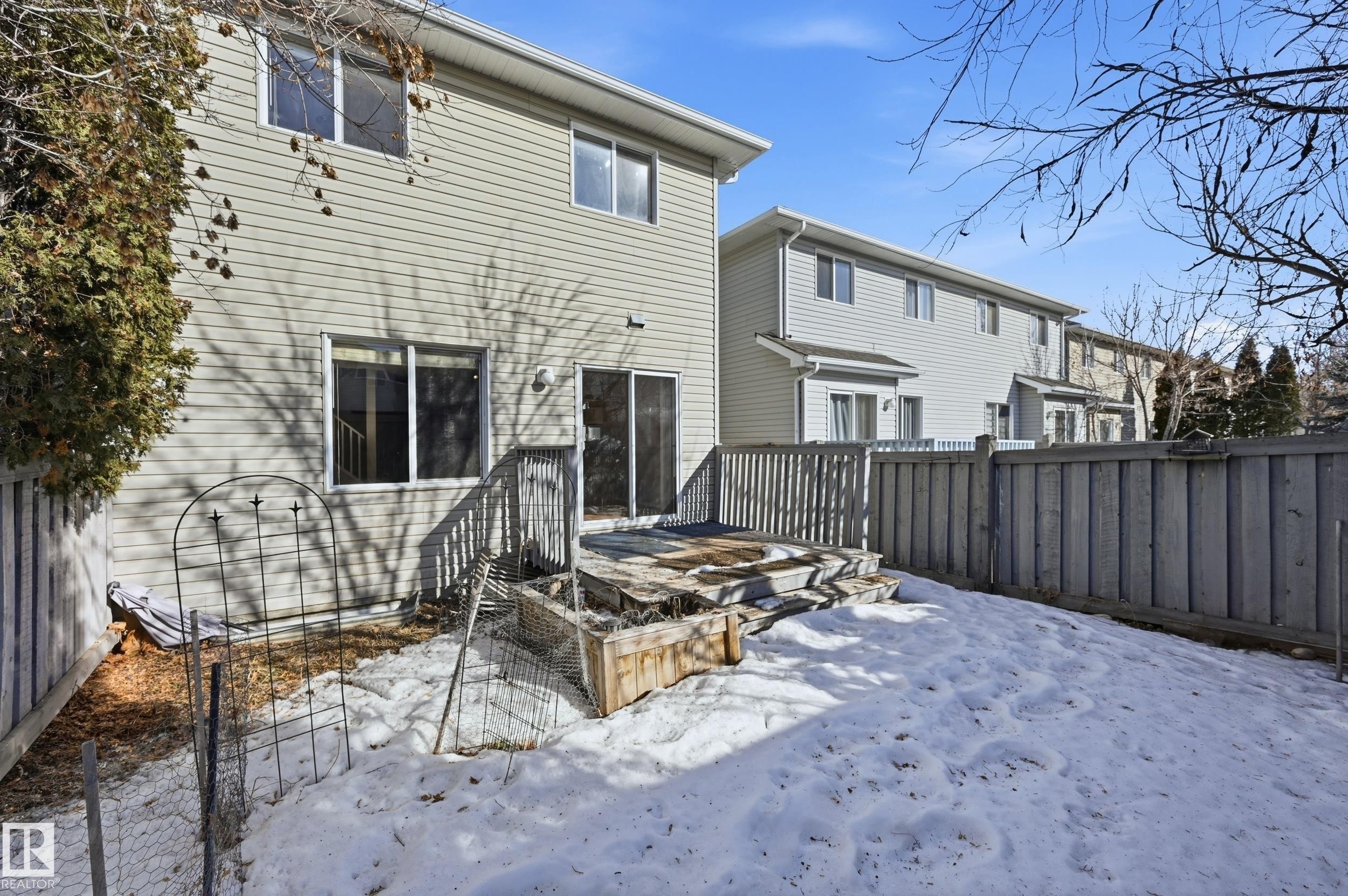The property features a rear exterior with light-colored siding and a wooden deck, accessible via sliding glass doors - 53 287 Macewan Road, Edmonton, AB - Outdoor