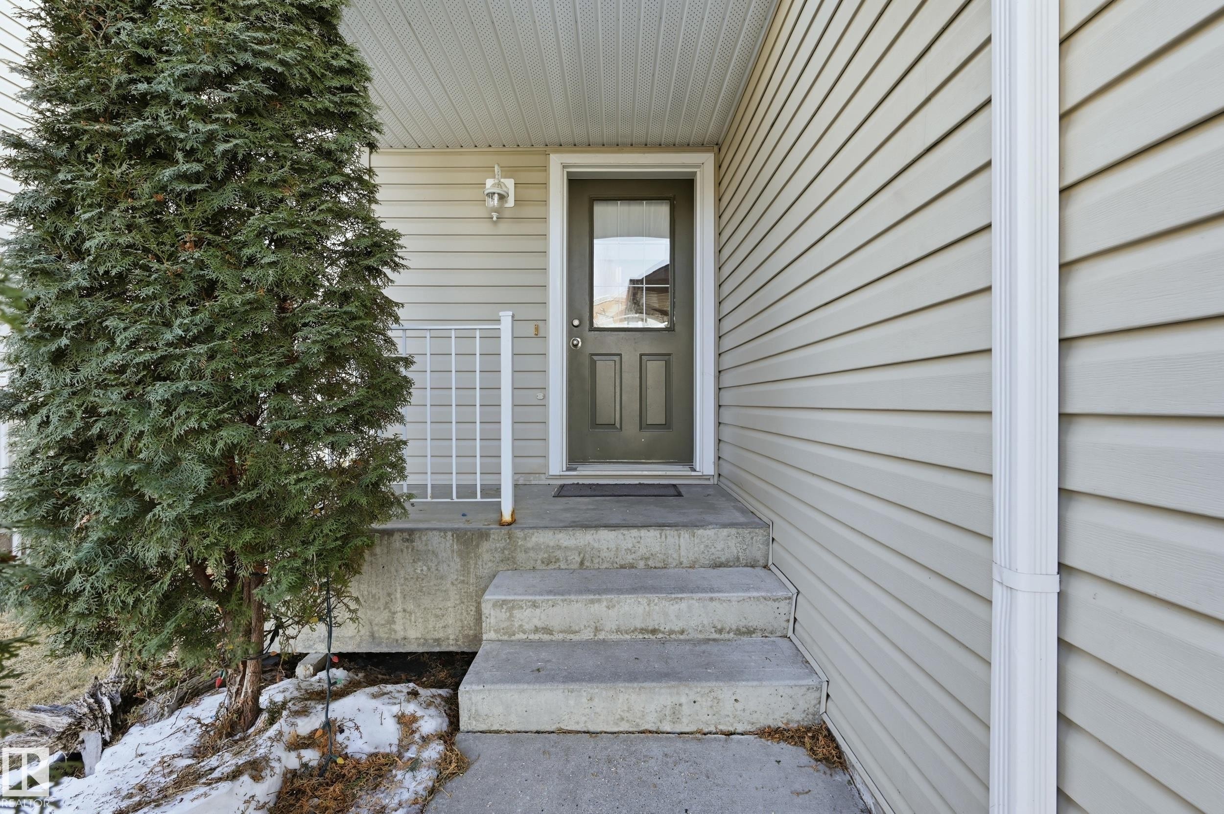 The property features a concrete front porch with steps, a dark-colored entry door with a glass insert, and light-colored siding - 53 287 Macewan Road, Edmonton, AB - Outdoor With Exterior