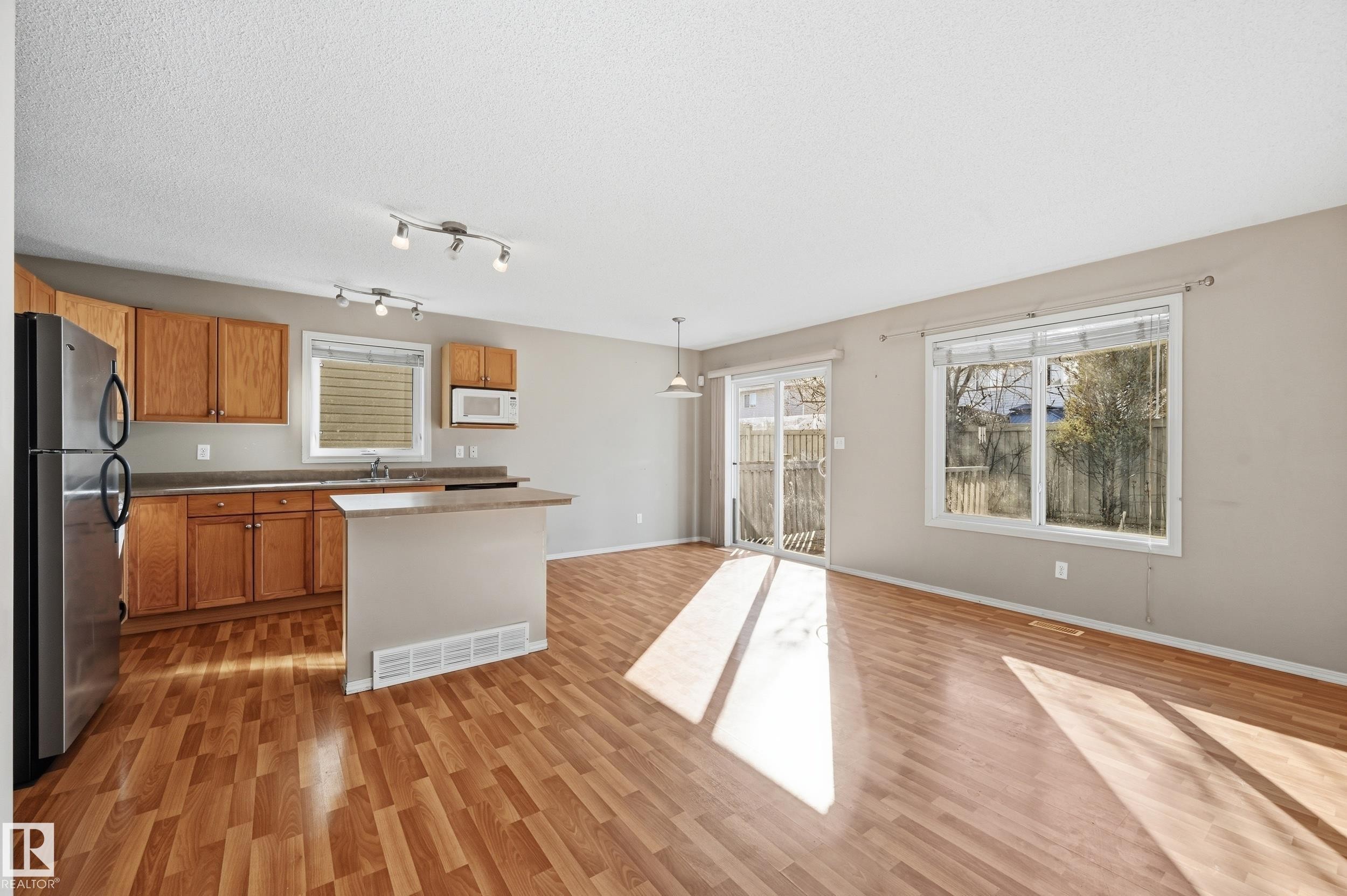 Open concept living area featuring wood laminate flooring and a kitchen with wooden cabinetry, a stainless steel refrigerator, and a kitchen island - 53 287 Macewan Road, Edmonton, AB - Indoor Photo Showing Kitchen