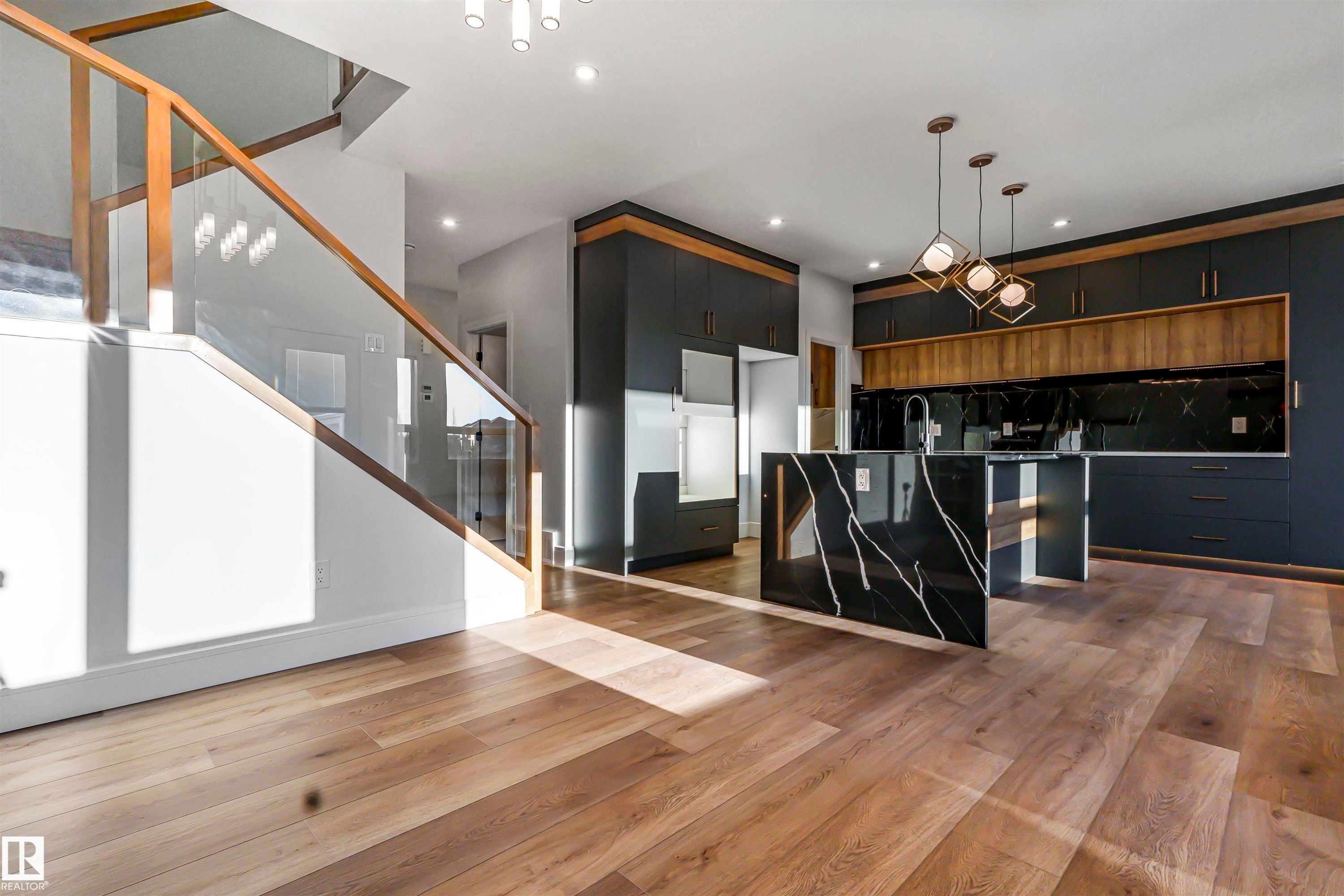 The property features hardwood floors throughout, a modern kitchen with dark cabinetry and a black marble-patterned island, and a staircase with glass panel railings - 368 Creekside Green, Leduc, AB - Indoor