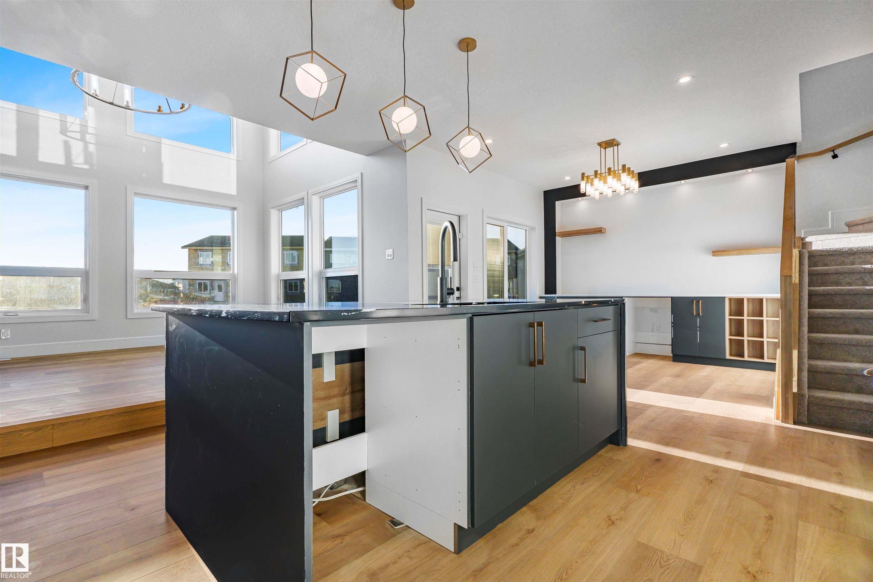 Modern kitchen featuring a large island with dark cabinetry and a stone countertop, complemented by contemporary light fixtures - 368 Creekside Green, Leduc, AB - Indoor Photo Showing Kitchen