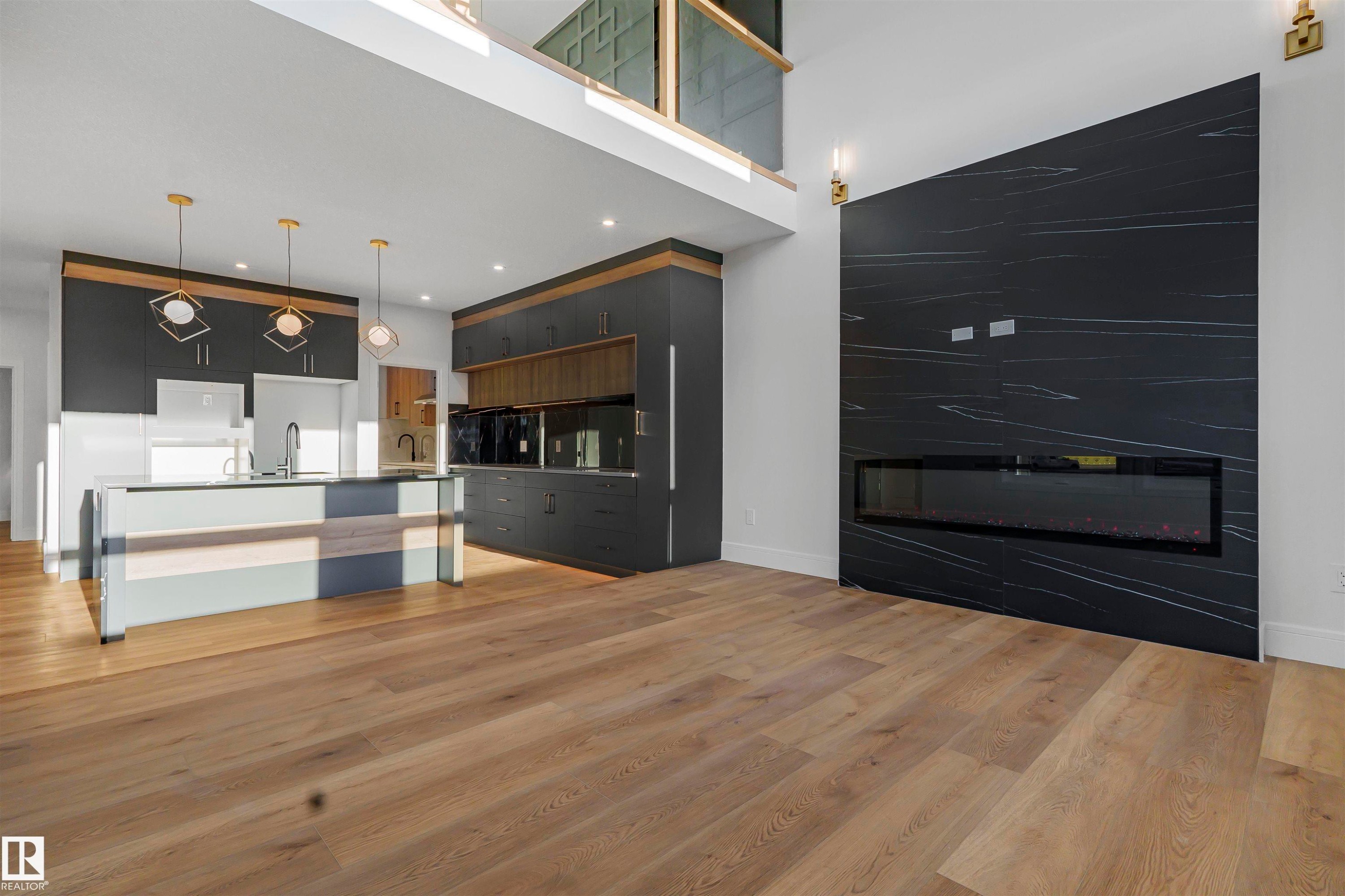 The open-concept interior features light wood-style flooring, a kitchen with dark cabinetry and a central island, and a fireplace with a dark, textured surround - 368 Creekside Green, Leduc, AB - Indoor With Fireplace