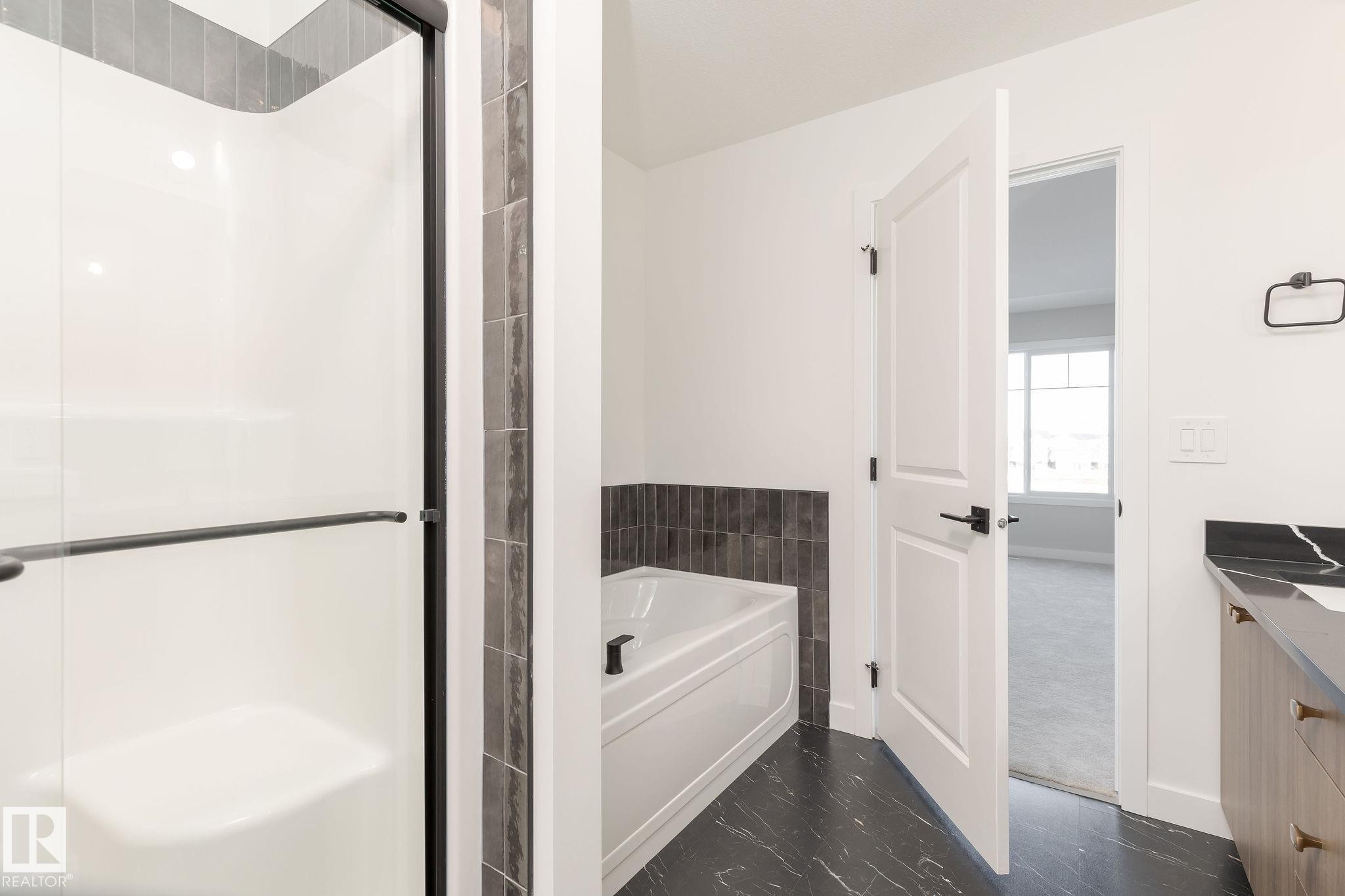 Bathroom featuring a stand-up shower with a clear glass enclosure, a white soaking tub with dark tile surround, and a vanity with a black countertop - 2206 Crossbill Link, Edmonton, AB - Indoor Photo Showing Bathroom