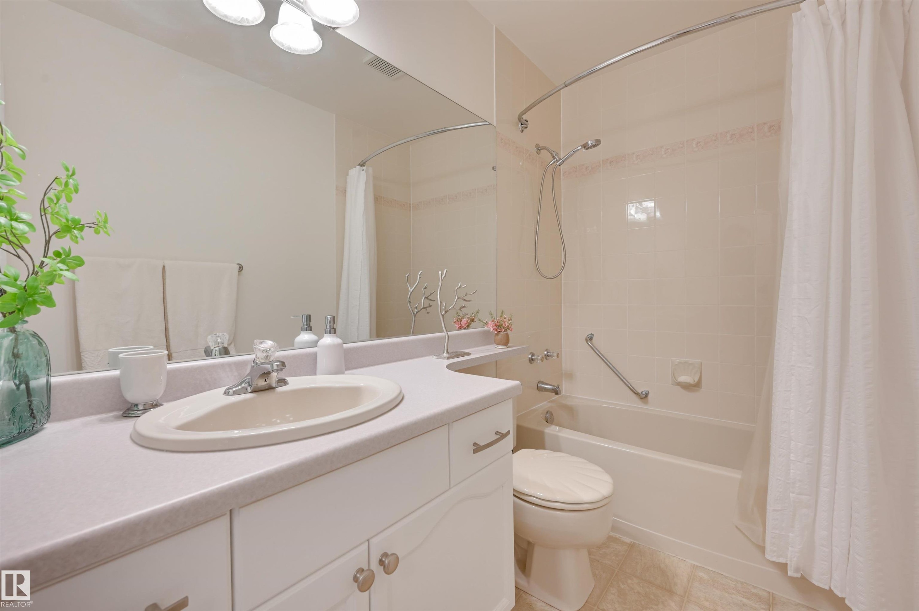 Bathroom featuring a vanity with an integrated sink and base cabinetry, a bathtub with a shower, and a large mirror - 304 17151 94A Avenue, Edmonton, AB - Indoor Photo Showing Bathroom