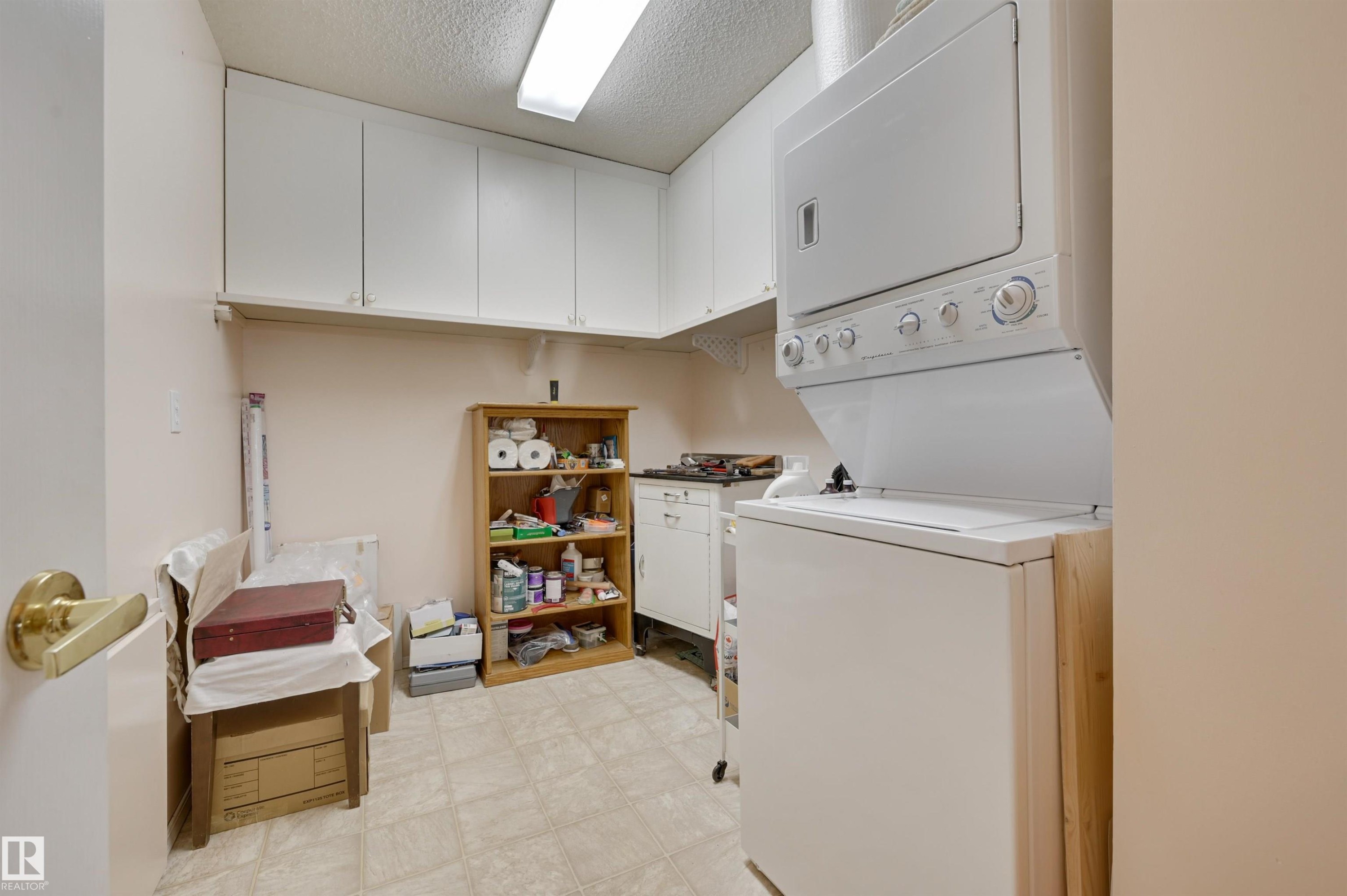 The utility area features a stacked washer and dryer, extensive upper cabinetry, and tiled flooring - 304 17151 94A Avenue, Edmonton, AB - Indoor Photo Showing Laundry Room