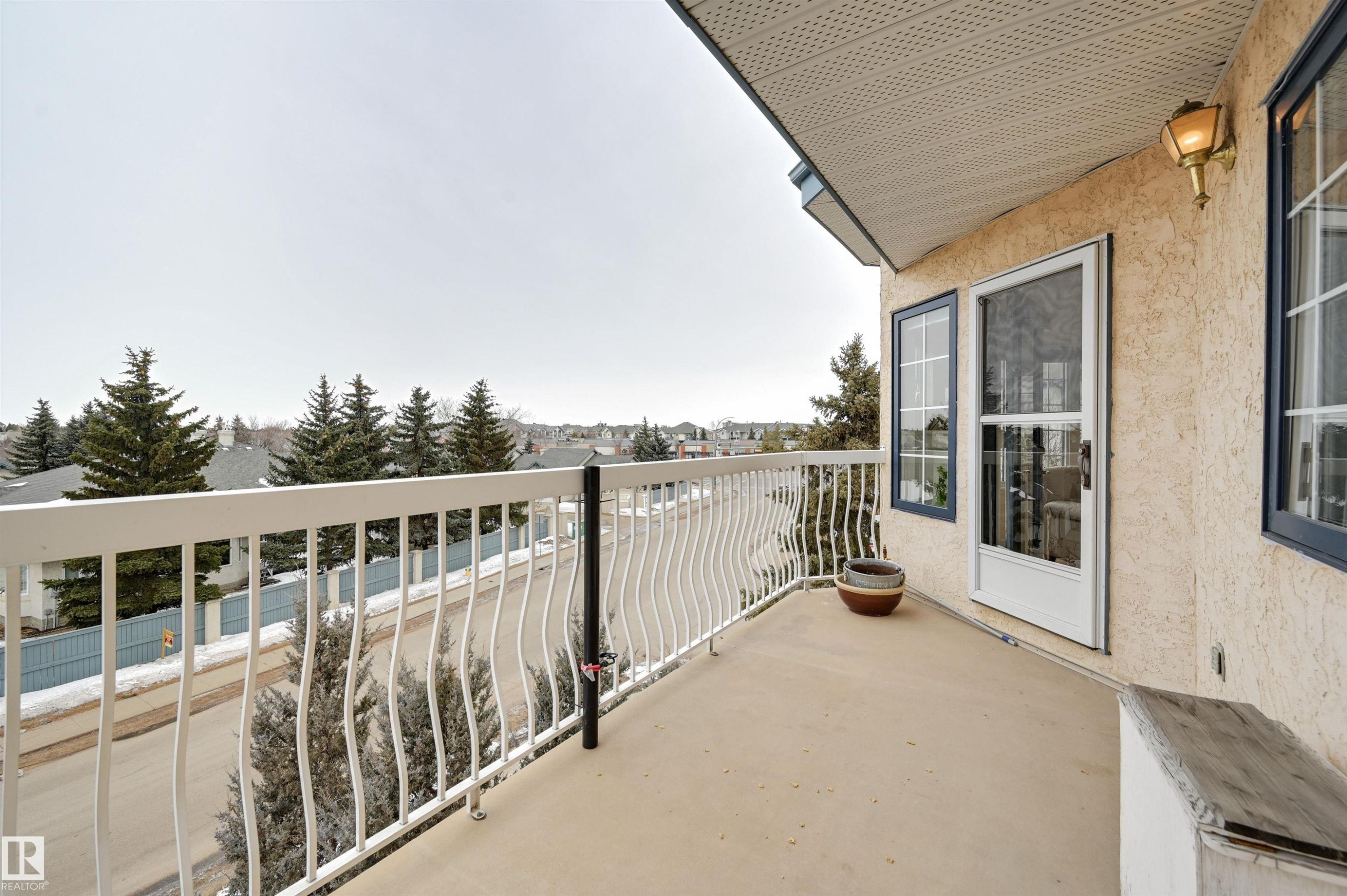 The property features an exterior balcony with a white railing, providing views of the surrounding neighborhood with visible trees and residential structures - 304 17151 94A Avenue, Edmonton, AB - Outdoor With Balcony With Exterior
