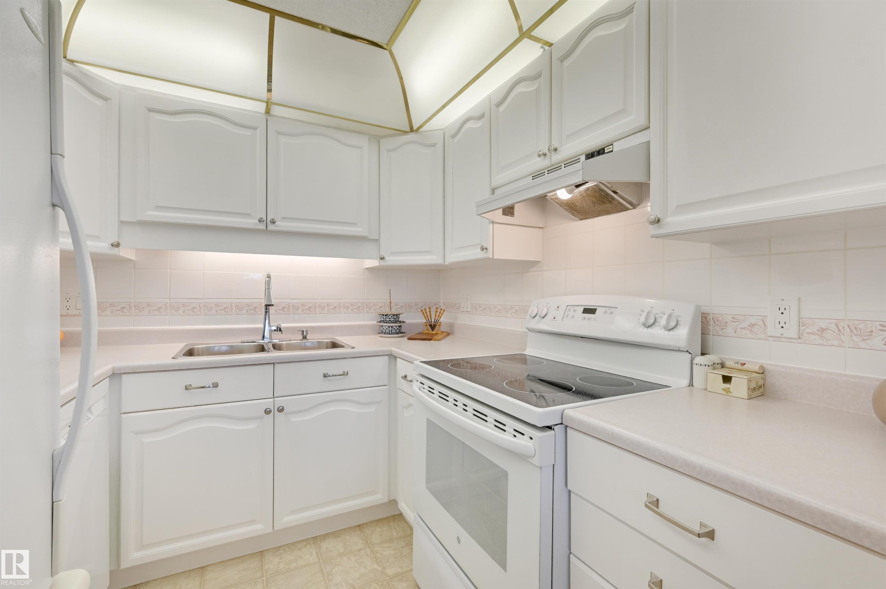 The kitchen features white cabinetry, a white countertop, and a white electric range with a cooktop - 304 17151 94A Avenue, Edmonton, AB - Indoor Photo Showing Kitchen With Double Sink