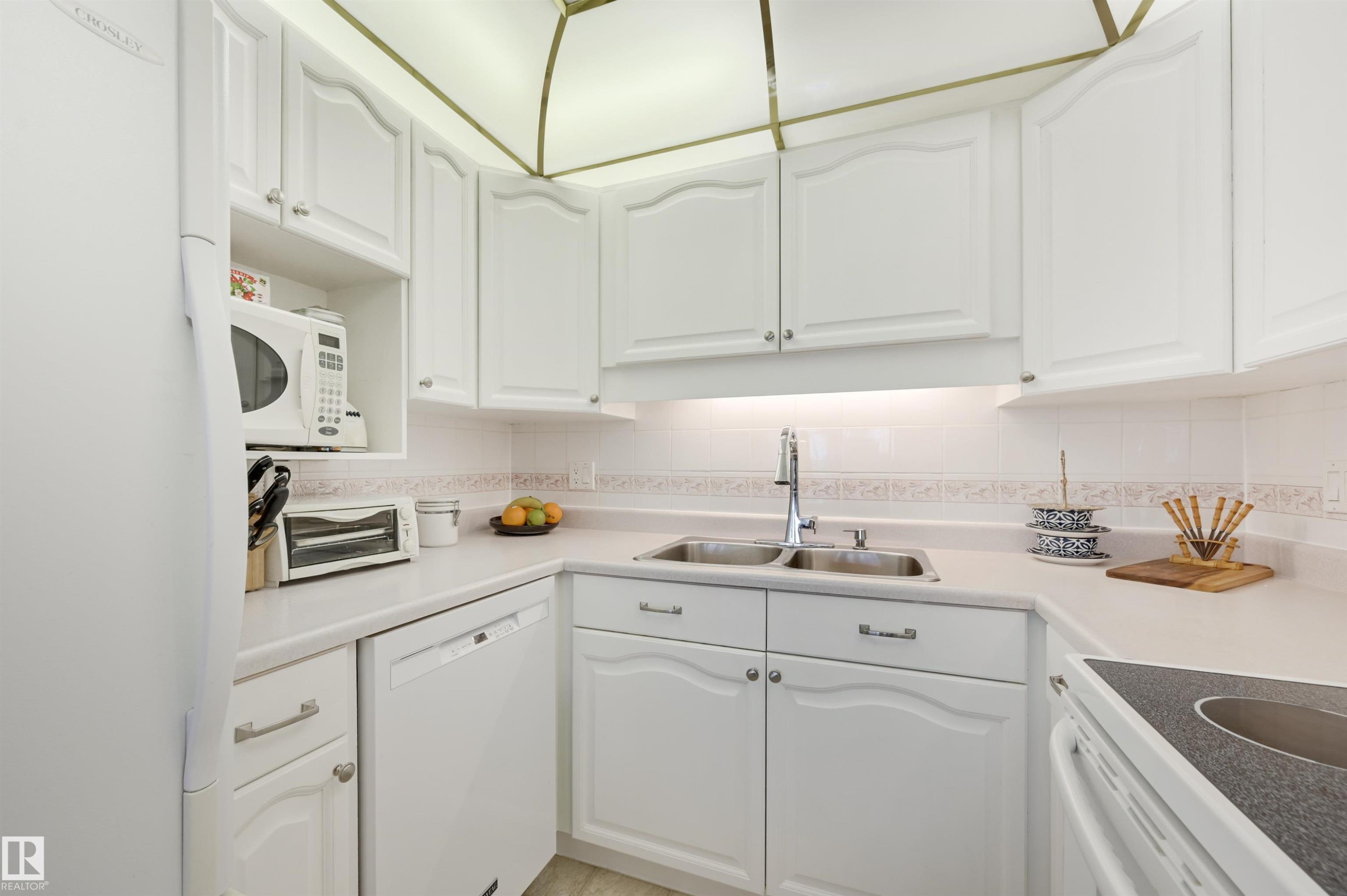 The kitchen features white cabinetry, a double basin sink with a chrome faucet, and integrated appliances - 304 17151 94A Avenue, Edmonton, AB - Indoor Photo Showing Kitchen With Double Sink