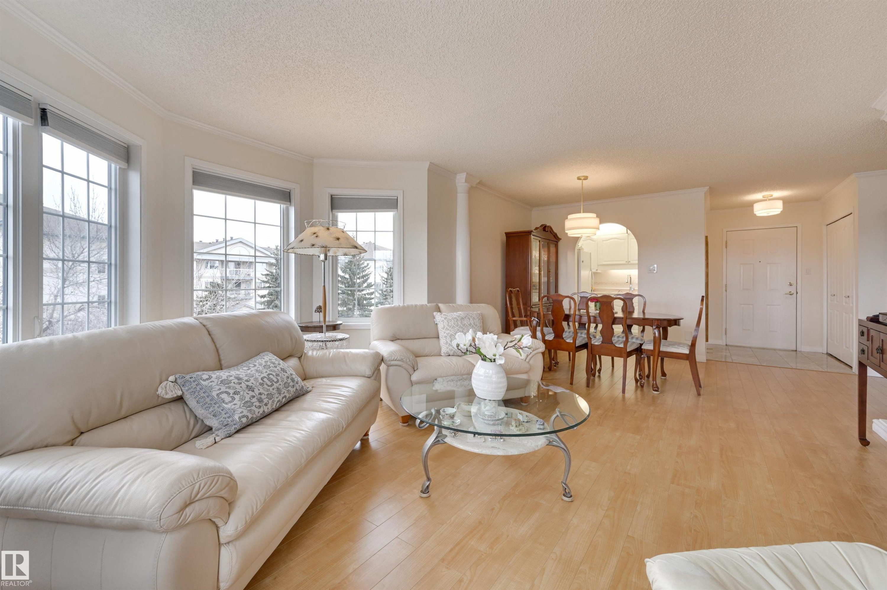 The living area features light-toned flooring, several windows providing natural light, and a dining area with a chandelier - 304 17151 94A Avenue, Edmonton, AB - Indoor Photo Showing Living Room