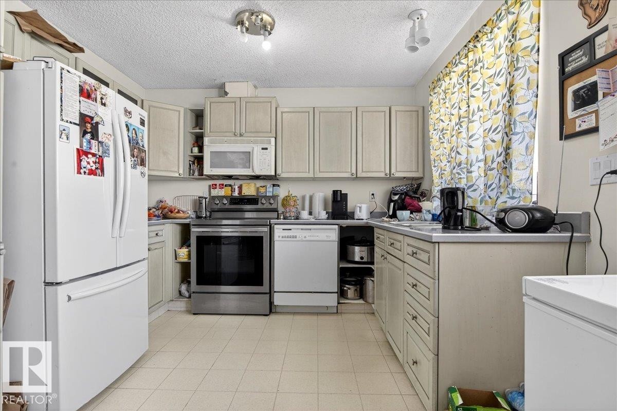The kitchen features light-colored cabinetry, a white refrigerator, a stainless steel range, and a white dishwasher - 13304 130 Avenue, Edmonton, AB - Indoor Photo Showing Other Room