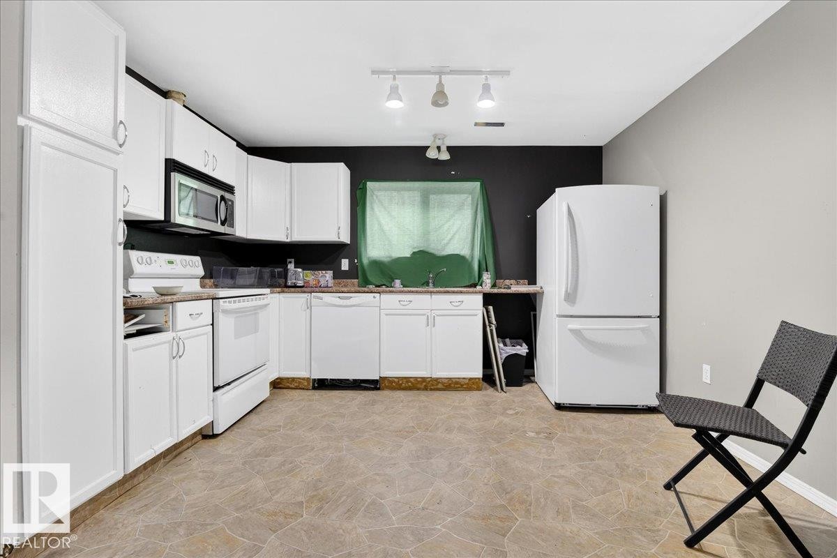 The kitchen features white cabinetry, white appliances, and track lighting - 13304 130 Avenue, Edmonton, AB - Indoor Photo Showing Kitchen