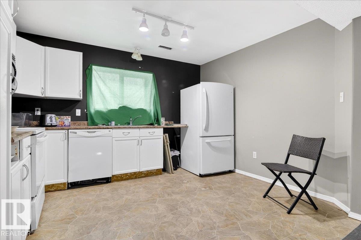 This kitchen features white cabinetry, a white refrigerator, a white dishwasher, and light-colored floor tiles - 13304 130 Avenue, Edmonton, AB - Indoor Photo Showing Laundry Room