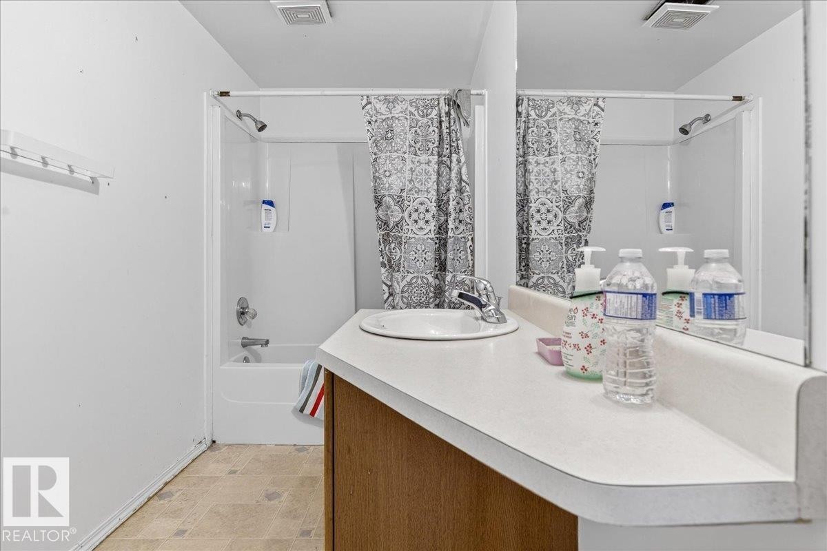 Bathroom featuring a vanity with an integrated sink and mirror, and a shower-over-tub combination with a shower curtain - 13304 130 Avenue, Edmonton, AB - Indoor Photo Showing Bathroom