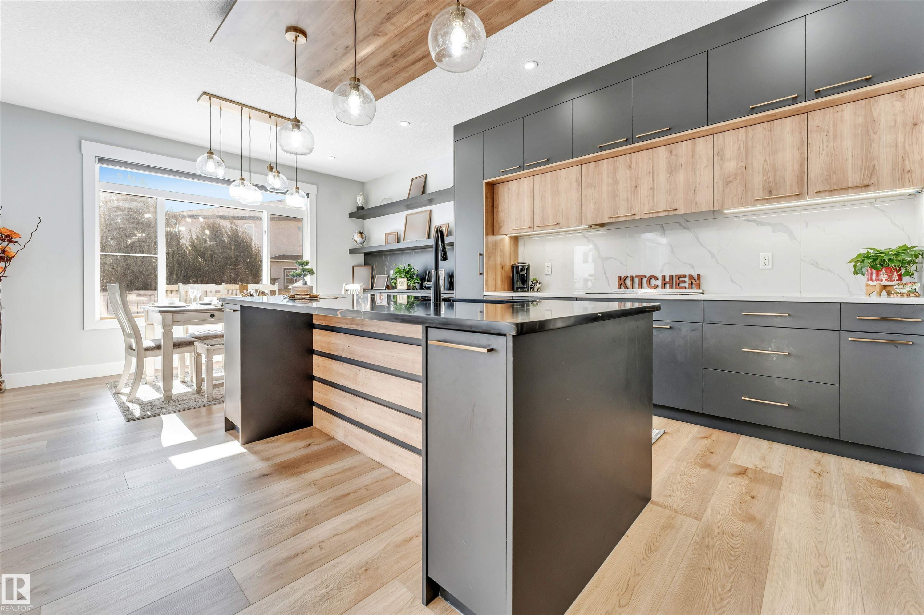 Kitchen featuring a large island with a dark countertop and wood accents, light hardwood floors, and extensive cabinetry in dark grey and light wood tones - 1531 151 Avenue, Edmonton, AB - Indoor Photo Showing Kitchen With Upgraded Kitchen
