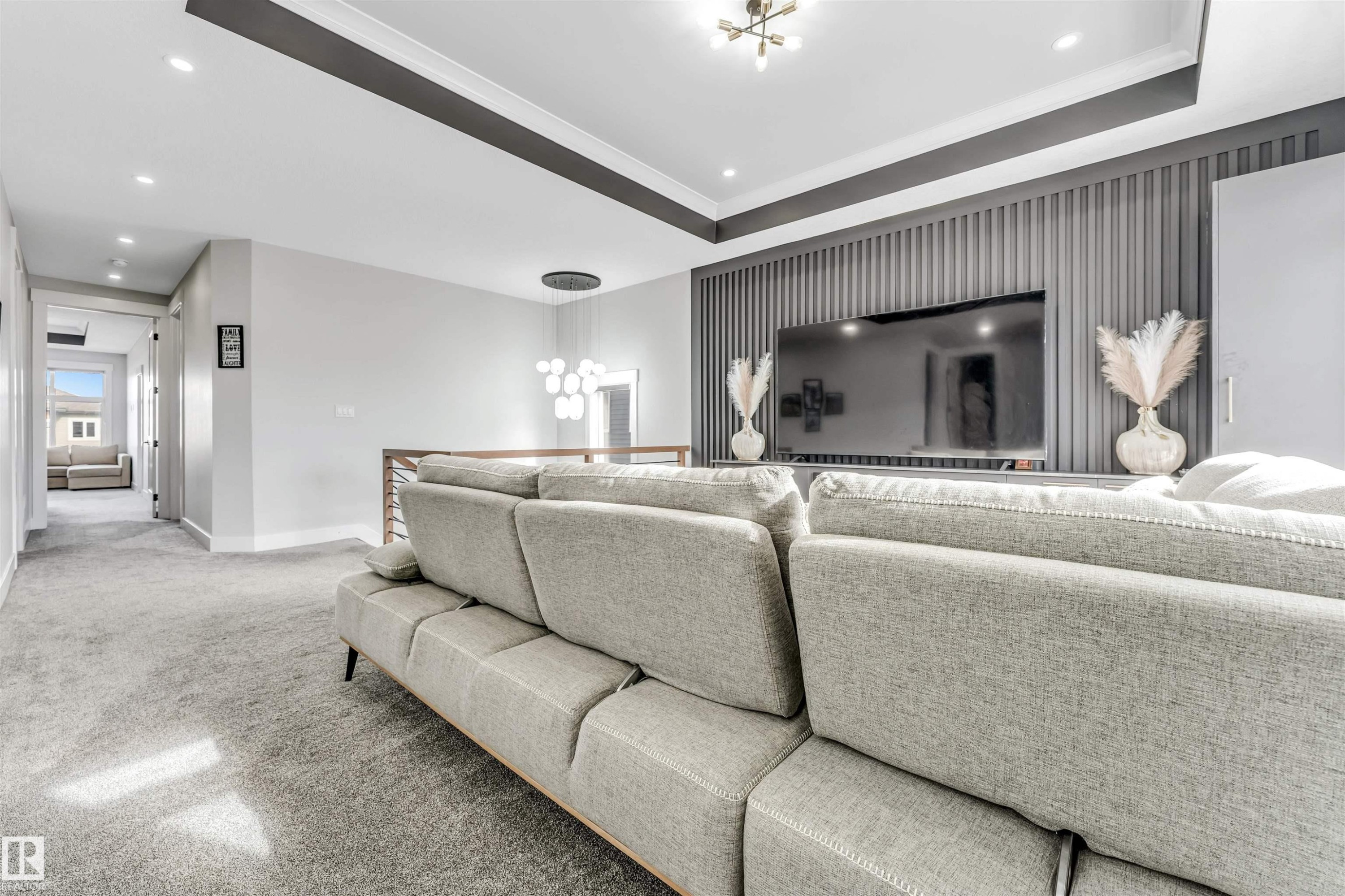 Spacious living area featuring carpeted flooring, a decorative accent wall with a mounted television, and a stylish ceiling light fixture - 1531 151 Avenue, Edmonton, AB - Indoor